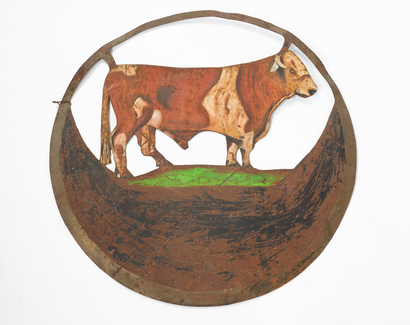 DOUBLE-SIDED SHEET METAL TRADE SIGN WITH SILHOUETTE OF BULL.: DOUBLE-SIDED SHEET METAL TRADE SIGN WITH SILHOUETTE OF BULL. American, first-half 20th Century. Circular sign, brown and white bull on green grass, gold border, and black lower field for sign.