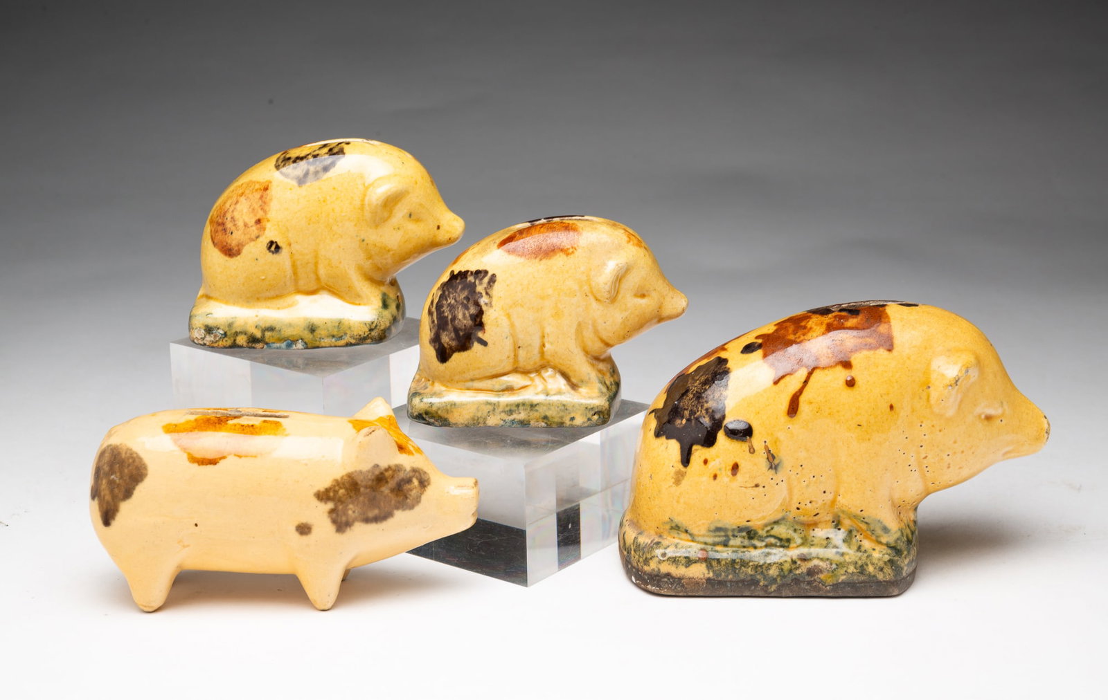 FOUR GLAZED POTTERY PIG BANKS.: FOUR GLAZED POTTERY PIG BANKS. American, Late 19th or Early 20th Century. Comprising three seated examples on sponge-glazed plinths and one free-standing pig. Some possibly Roseville. Largest, 4"h.