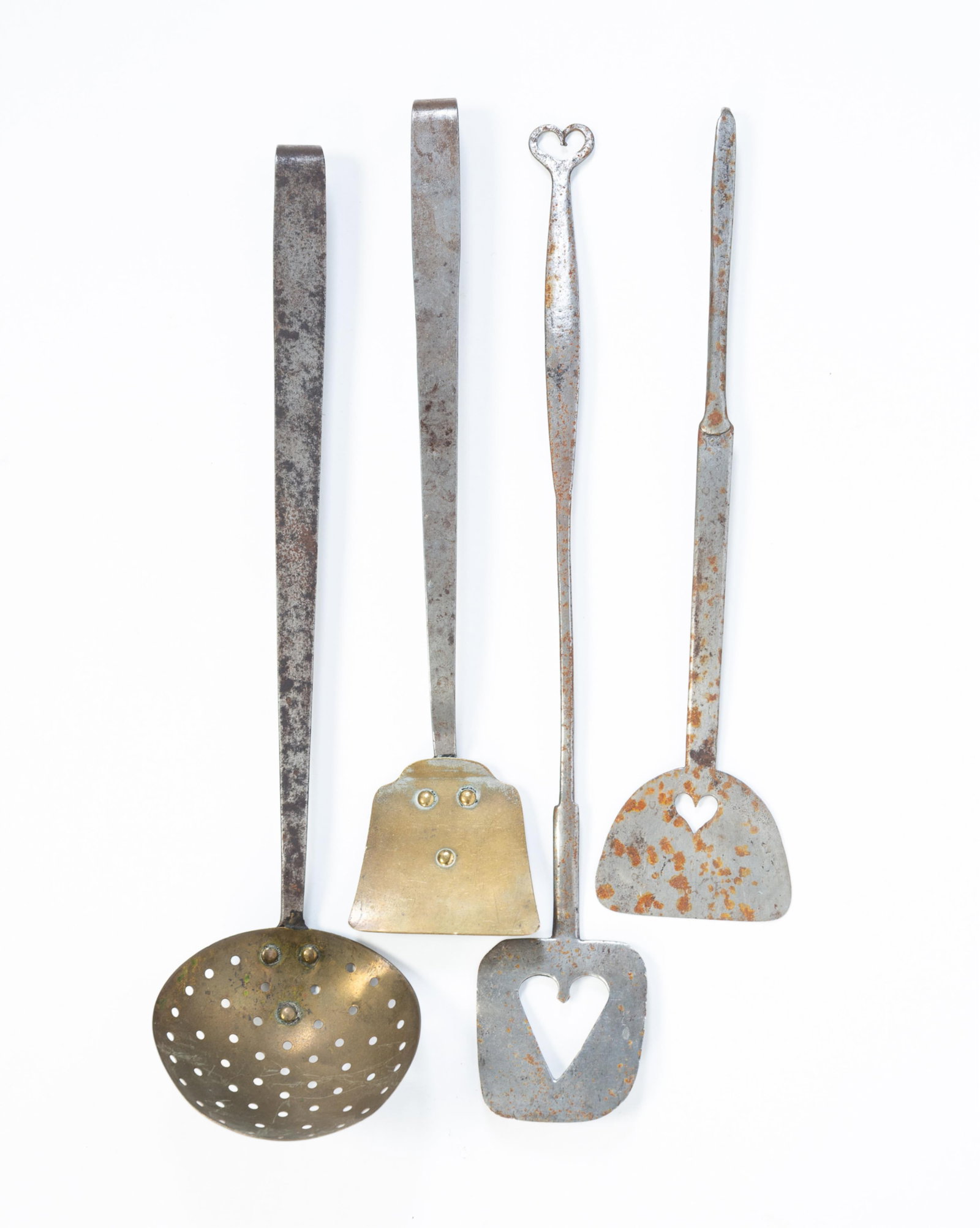 FOUR METAL HEARTHSIDE UTENSILS, TWO WITH HEART CUTOUTS.: FOUR METAL HEARTHSIDE UTENSILS, TWO WITH HEART CUTOUTS. American, 19th Century. Two steel spatulas with heart cutouts, one of demilune form and one rounded square form with a heart hook at end of