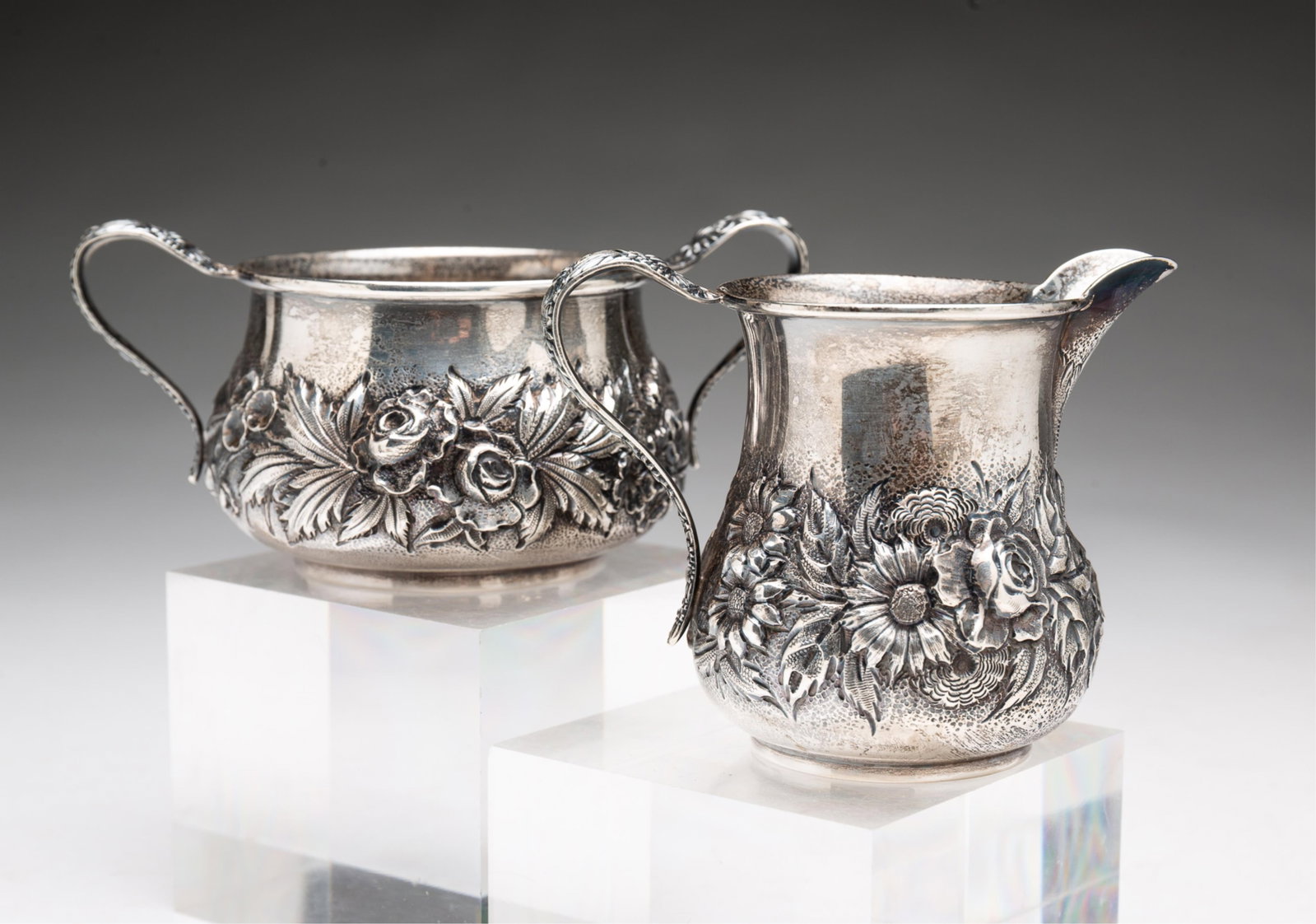 KIRK AND SON STERLING SILVER REPOUSSE CREAMER AND OPEN SUGAR.: KIRK AND SON STERLING SILVER REPOUSSE CREAMER AND OPEN SUGAR. American, Early 20th Century. Hand-chased floral pattern with leaf brackets. Marked to bottom. Creamer, 3.25"h. Sugar, 2.25"h.