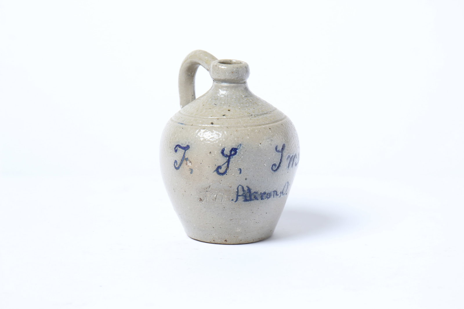 DIMINUTIVE COBALT-DECORATED STONEWARE JUG, INSCRIBED "T.S. SMITH AKRON, O.": DIMINUTIVE COBALT-DECORATED STONEWARE JUG, INSCRIBED "T.S. SMITH AKRON, O." American (Ohio), 19th Century. With molded spout, tooled shoulder, and applied handle; 4.75"h. Provenance: Nancy Goff (Allia