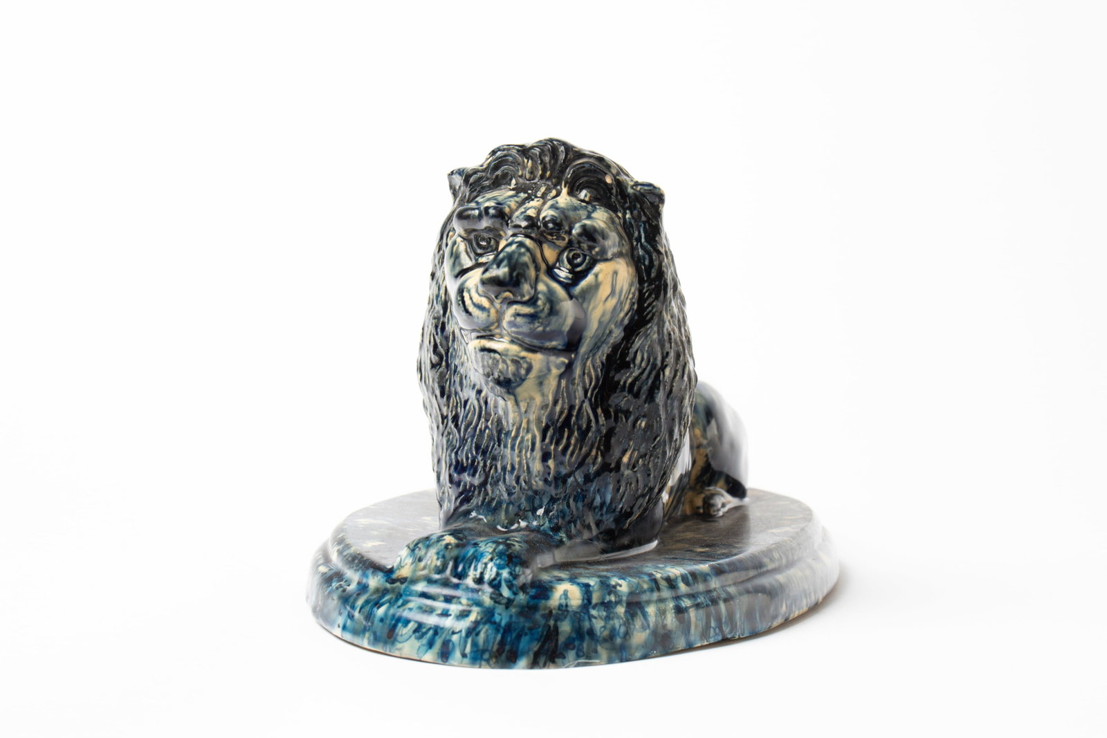 FINE LARGE MOGADORE, OHIO BUFF CLAY RECLINING LION WITH UNUSUAL BLUE GLAZE.: FINE LARGE MOGADORE, OHIO BUFF CLAY RECLINING LION WITH UNUSUAL BLUE GLAZE. American, 19th Century. Lion with blue and white body and incised mane lying atop a mottled, stepped, and oval base. 8"h.