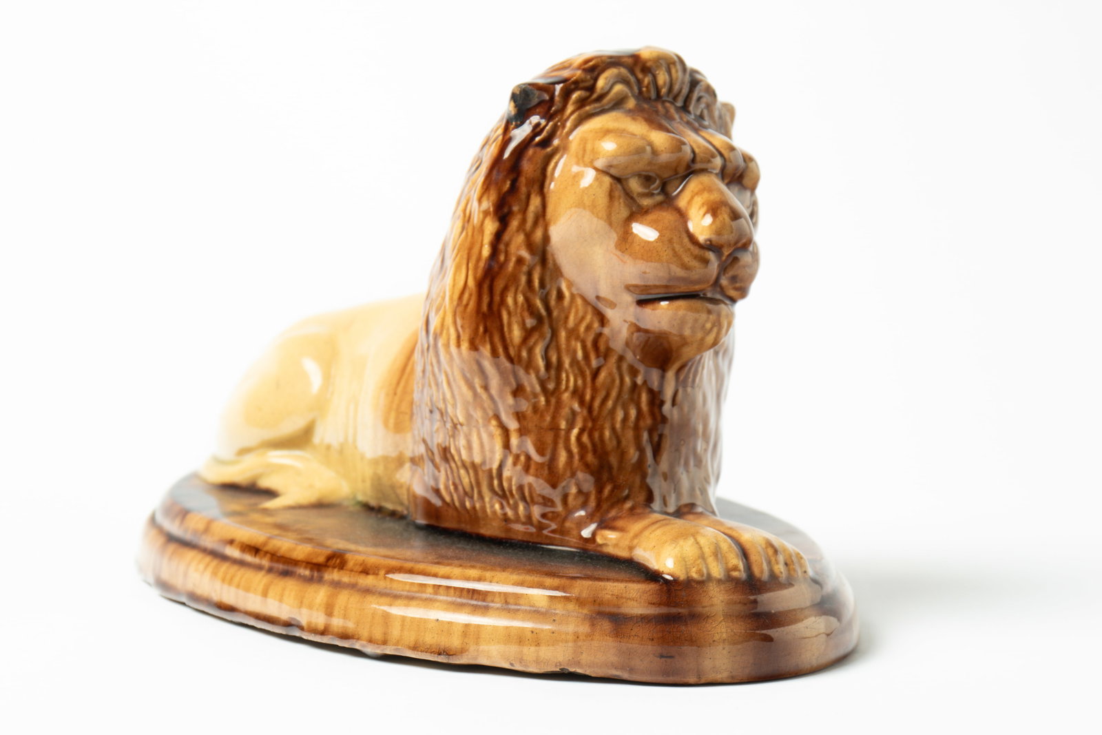 FINE LARGE MOGADORE, OHIO, BUFF CLAY RECLINING LION WITH YELLOW AND BROWN GLAZE.: FINE LARGE MOGADORE, OHIO, BUFF CLAY RECLINING LION WITH YELLOW AND BROWN GLAZE. American, 19th Century. Lion with yellow body and molded brown mane lying atop a mottled, stepped, and oval base.