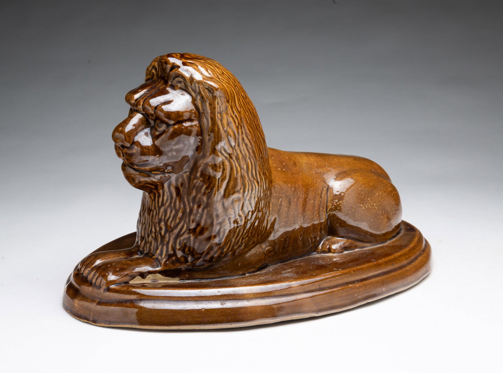 AKRON, OHIO BUFF CLAY RECLINING LION WITH BROWN GLAZE, SIGNED "ISABELLE QUIROS.": AKRON, OHIO BUFF CLAY RECLINING LION WITH BROWN GLAZE, SIGNED "ISABELLE QUIROS." American, 19th Century. Lion with brown glaze lying atop a stepped oval base. Marked "Isabelle Quiros / Akron / May