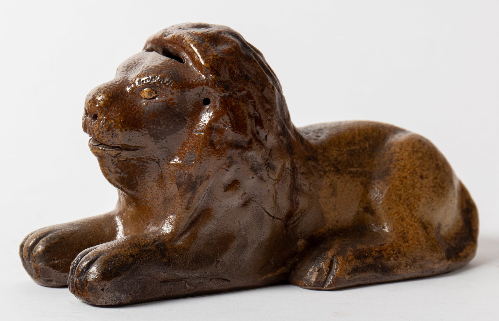 UNUSUAL PAINTED STONEWARE LION BANK WITH POTTERY EYES.: UNUSUAL PAINTED STONEWARE LION BANK WITH POTTERY EYES. American (possibly Ohio), 19th Century. Of recumbent form and with molded features; top of head with horizontal coin slot; applied pottery eyes; 