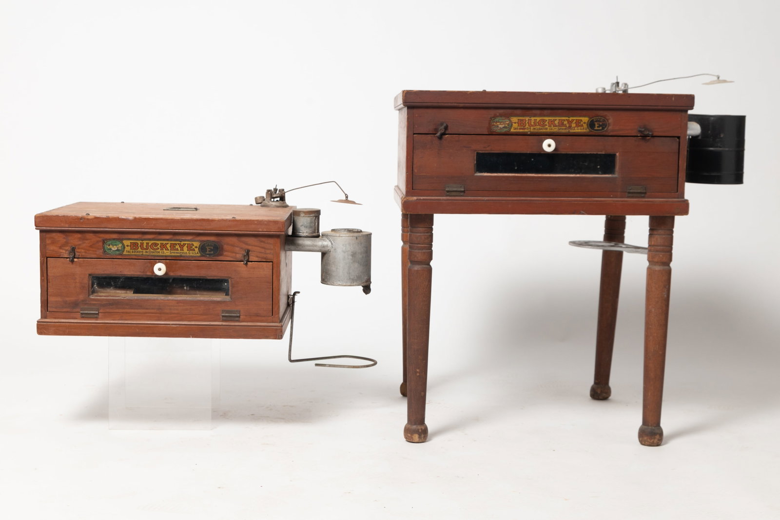 TWO SPRINGFIELD, OHIO "BUCKEYE INCUBATORS".: TWO SPRINGFIELD, OHIO "BUCKEYE INCUBATORS". American, early 20th Century. Pine. Both are "Style E", bead board tops, hinged doors with windows on front, metal heaters, and decal labels "BUCKEYE, THE