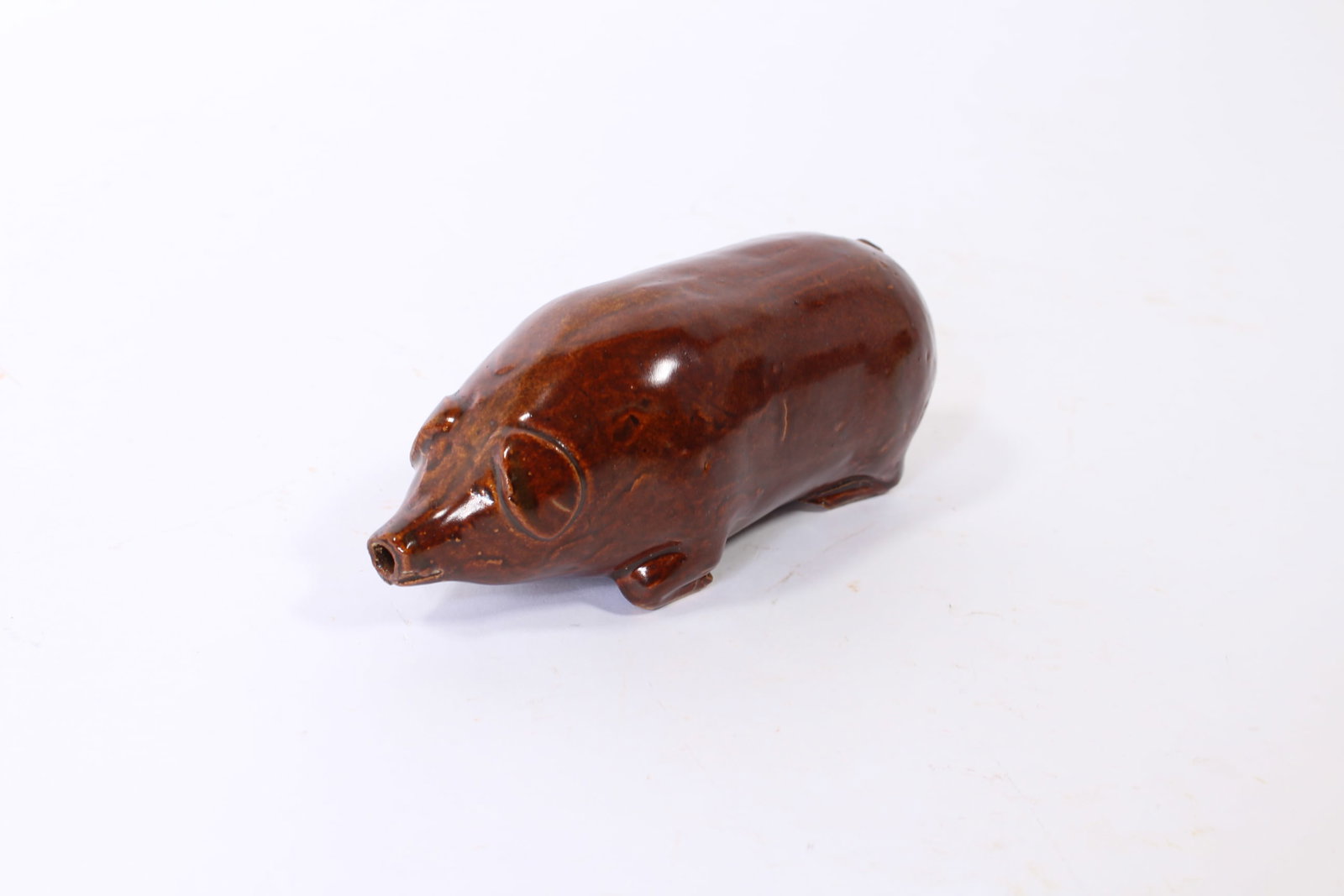 MONMOUTH, ILLINOIS ALBANY-GLAZED STONEWARE PIG.: MONMOUTH, ILLINOIS ALBANY-GLAZED STONEWARE PIG. American, late 19th or early 20th Century. Depicting a reclining pig with legs below belly, with applied ears and tail. 2.5"h. 2.5"w. 6.5"l.