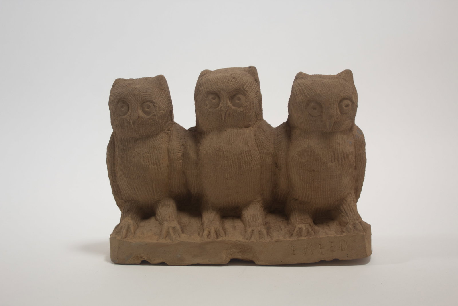 ERNEST "POPEYE" REED (OHIO, 1919 - 1985) FOLK ART CARVED STONE OWLS ON A BRANCH SCULPTURE.: ERNEST "POPEYE" REED (OHIO, 1919 - 1985) FOLK ART CARVED STONE OWLS ON A BRANCH SCULPTURE. American, 20th Century. Signed to front. A rectangular plinth holing three owls in a row with wide eyes and t