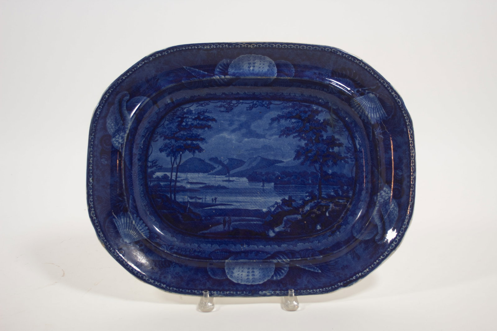 ENOCH WOOD AND SONS HISTORICAL BLUE PLATTER "LAKE GEORGE, STATE OF NEW YORK.": ENOCH WOOD AND SONS HISTORICAL BLUE PLATTER "LAKE GEORGE, STATE OF NEW YORK." England, mid- 19th Century. View of the lake with boats on the water and people in foreground, shell border, and