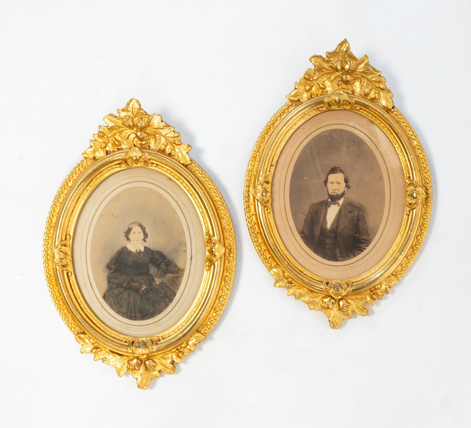 PAIR OF SMITH & CLARK (HARRISBURG, PENNSYLVANIA) EMBELLISHED PHOTOGRAPH PORTRAITS OF HUSBAND AND: PAIR OF SMITH & CLARK (HARRISBURG, PENNSYLVANIA) EMBELLISHED PHOTOGRAPH PORTRAITS OF HUSBAND AND WIFE IN OVAL GILT FRAMES. American, late 19th or early 20th Century. He wears a beard, a white shirt, a