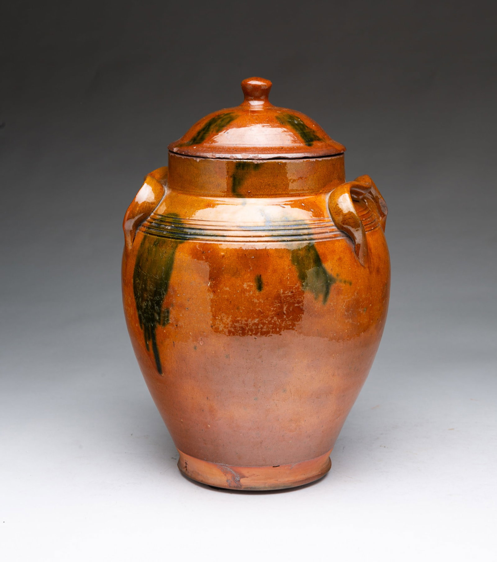 UNUSUAL NEW ENGLAND TWO-HANDLED LIDDED GLAZED REDWARE JAR WITH GREEN DRIPS.: UNUSUAL NEW ENGLAND TWO-HANDLED LIDDED GLAZED REDWARE JAR WITH GREEN DRIPS. American, 19th Century. Of ovoid form with dome lid with finial, high neck, serpentine lug handles, and tooled shoulder, in