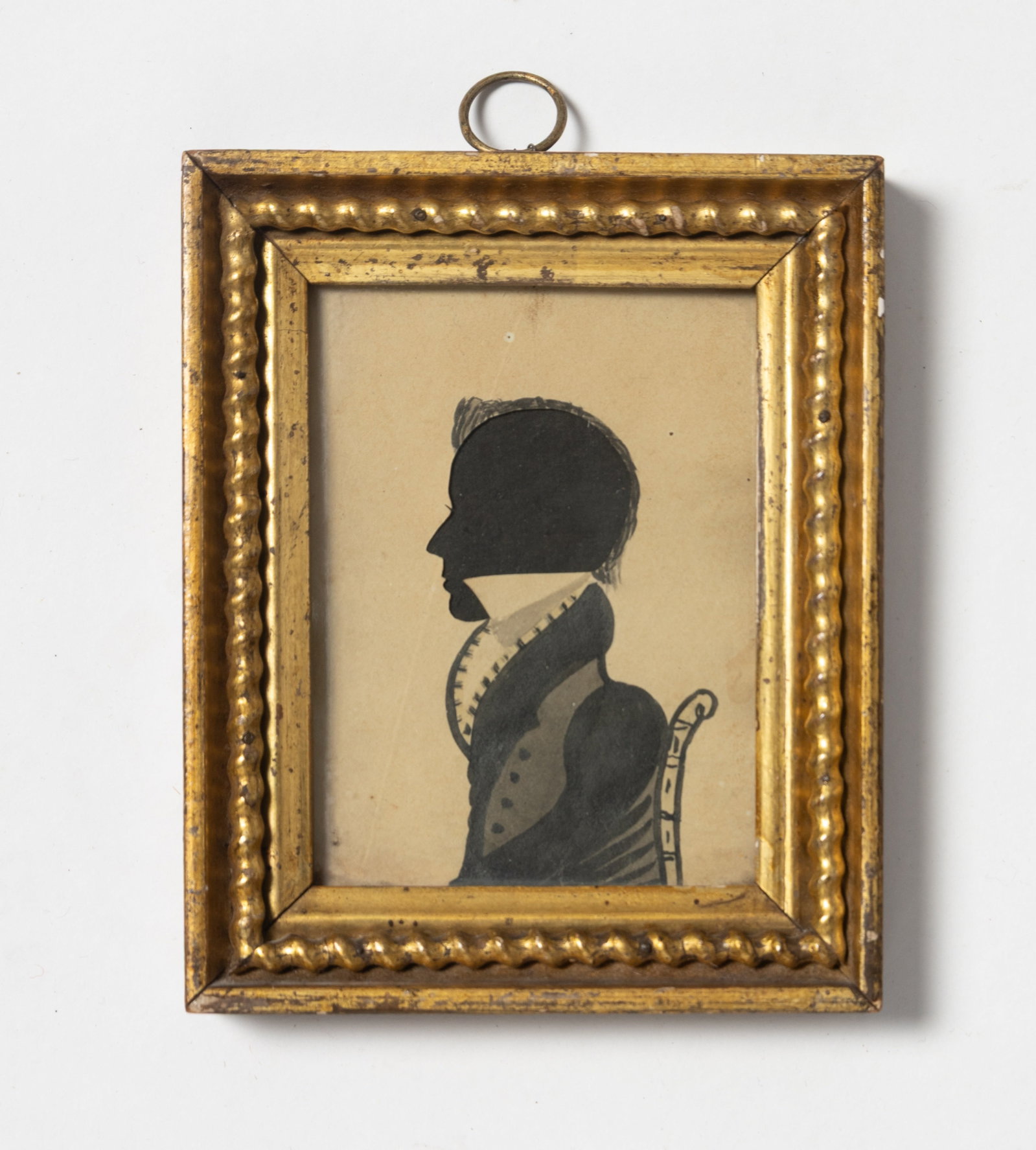 HOLLOW CUT PAPER AND WATERCOLOR SILHOUETTE PORTRAIT BUST OF A YOUNG MAN IN A CHAIR.: HOLLOW CUT PAPER AND WATERCOLOR SILHOUETTE PORTRAIT BUST OF A YOUNG MAN IN A CHAIR. American, 19th Century. Cut paper, ink, and watercolor. Side profile of a young gentleman with inked hair, stylish j