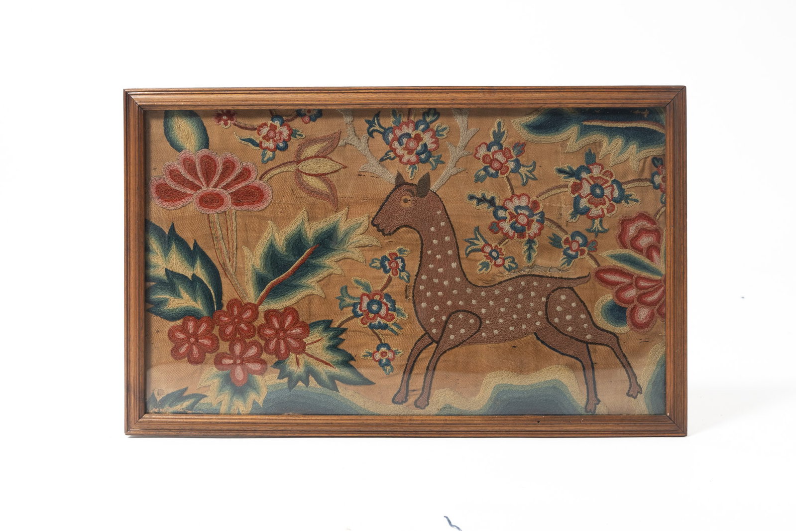 FRAMED CREWELWORK PANEL WITH A STAG.: FRAMED CREWELWORK PANEL WITH A STAG. American, 18th Century. Depiction of a large stag amid a sea of flowers and leaves. In a wooden frame behind glass, 14"h. 22.75"w. Provenance: Nancy Goff