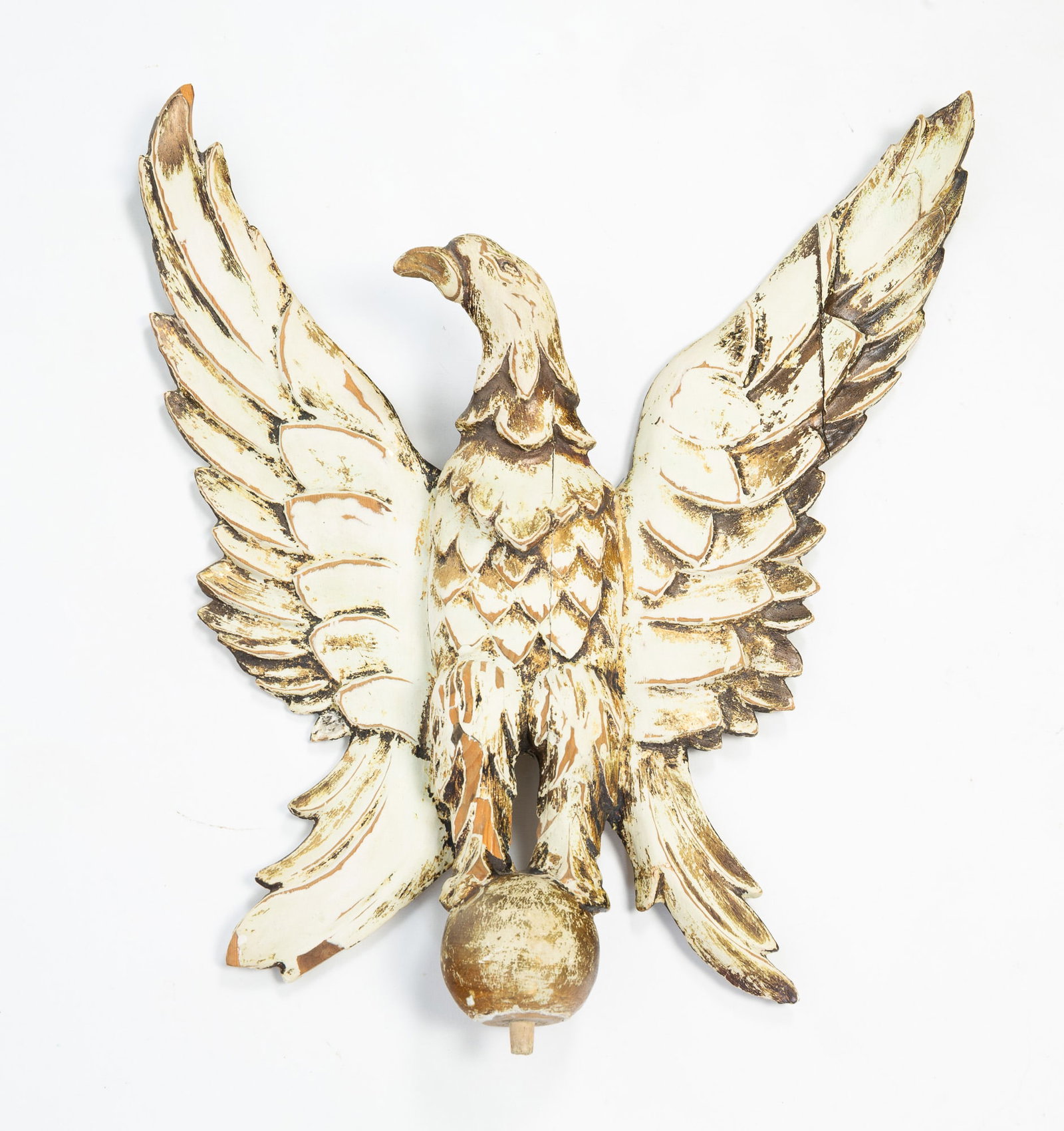 CARVED, PAINTED, AND PARCEL-GILT EAGLE.: CARVED, PAINTED, AND PARCEL-GILT EAGLE. American, 19th Century. Eagle with head turned to the right, spread wings, and perched on a ball, with later cream, black, and gold paint. 21.5"h. 17.5"w.