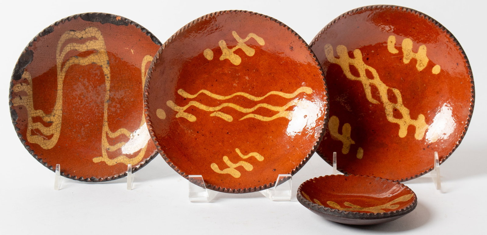 FOUR DIMINUTIVE SLIP-DECORATED REDWARE PLATES.: FOUR DIMINUTIVE SLIP-DECORATED REDWARE PLATES. American, 19th Century. Each with orange and brown mottled glaze, squiggles and wavy lines in yellow slip decoration, and coggled rim. Largest, 6.5"d.