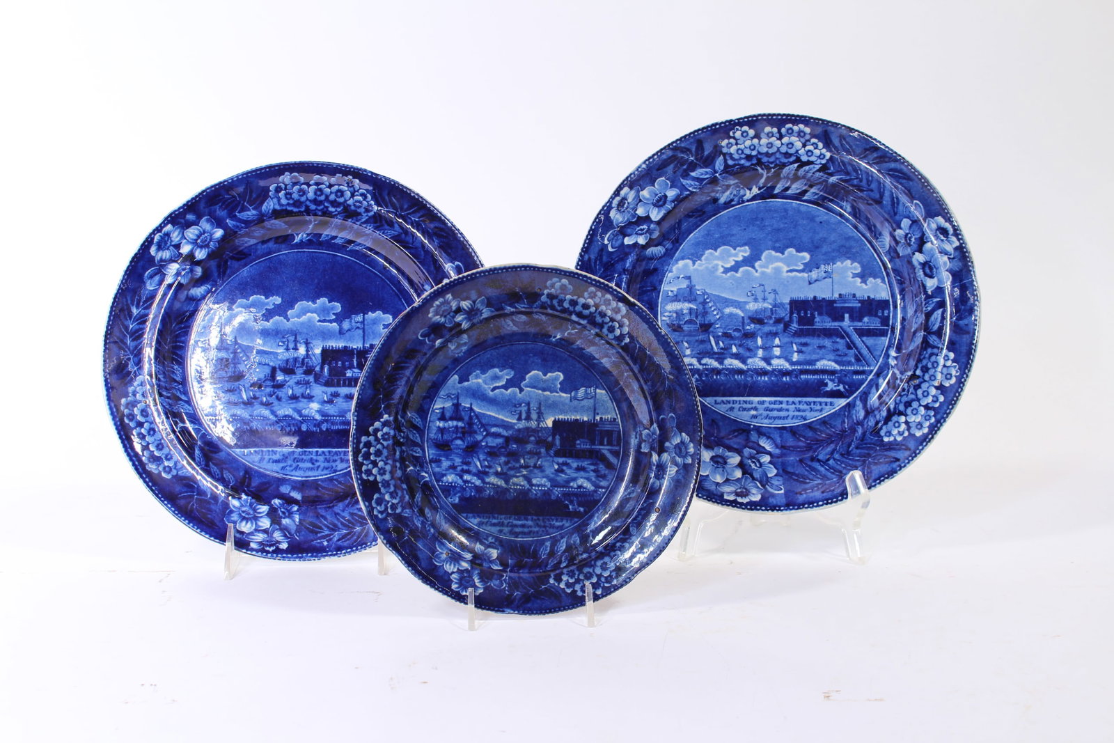 THREE CLEWS HISTORICAL BLUE LAFAYETTE PLATES.: THREE CLEWS HISTORICAL BLUE LAFAYETTE PLATES. England, mid- 19th Century. Floral borders with central scene "LANDING OF GEN. LAFAYETTE at Castle Garden, New York, 16th August 1824". Impressed mark on
