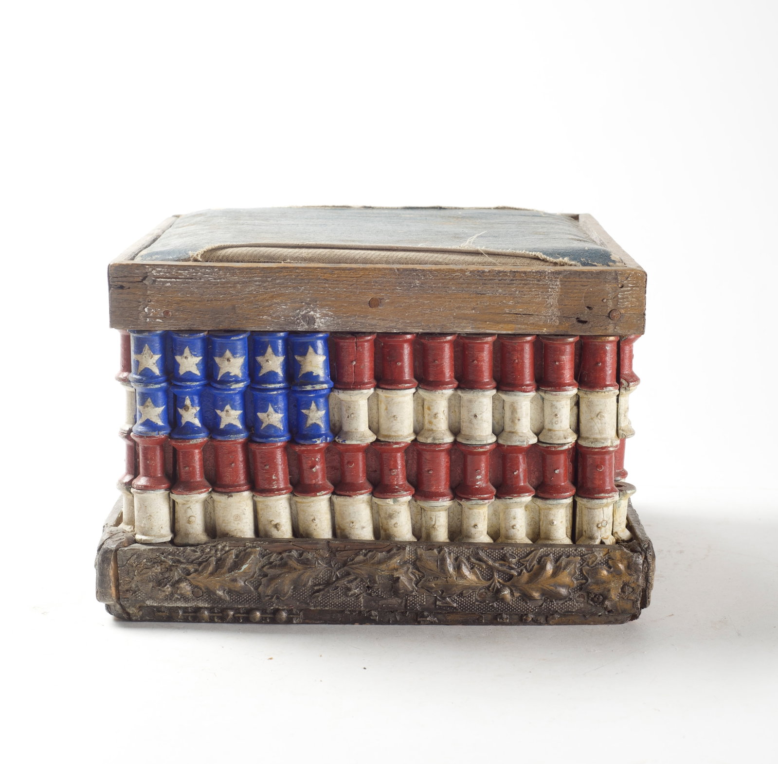 FOLK ART WOODEN FOOTSTOOL WITH PAINTED THREAD SPOOLS PAINTED LIKE THE AMERICAN FLAG IN RED, WHITE,: FOLK ART WOODEN FOOTSTOOL WITH PAINTED THREAD SPOOLS PAINTED LIKE THE AMERICAN FLAG IN RED, WHITE, AND BLUE. American, 20th Century. Blue leather top within a square wood frame over four sides of