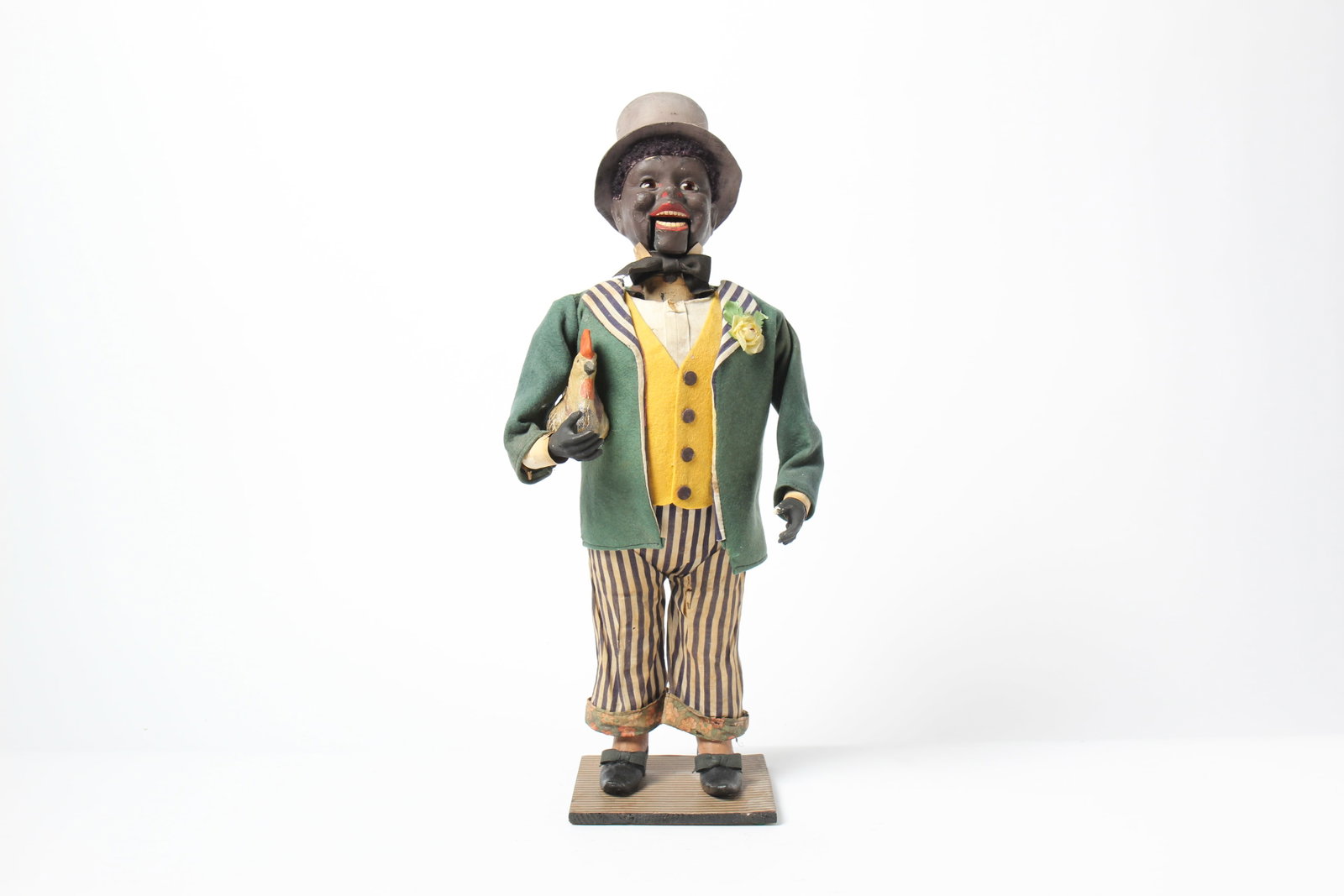 CLOCKWORK FIGURE HOLDING A CHICKEN.: CLOCKWORK FIGURE HOLDING A CHICKEN. Germany, Early 20th Century. A standing black man wearing a green jacket, yellow felt vest, white shirt, striped pants with floral cuffs, black composition shoes, a