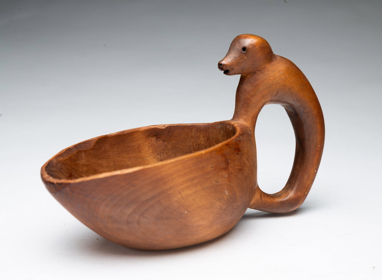 NATIVE AMERICAN CARVED EFFIGY CUP.: NATIVE AMERICAN CARVED EFFIGY CUP. 19th Century. Hardwood. Oval cup with an elongated top rim and a handle carved as an animal with pierced eyes and nostrils and an open mouth. 4.25"h. 3"w. 6.75"d.