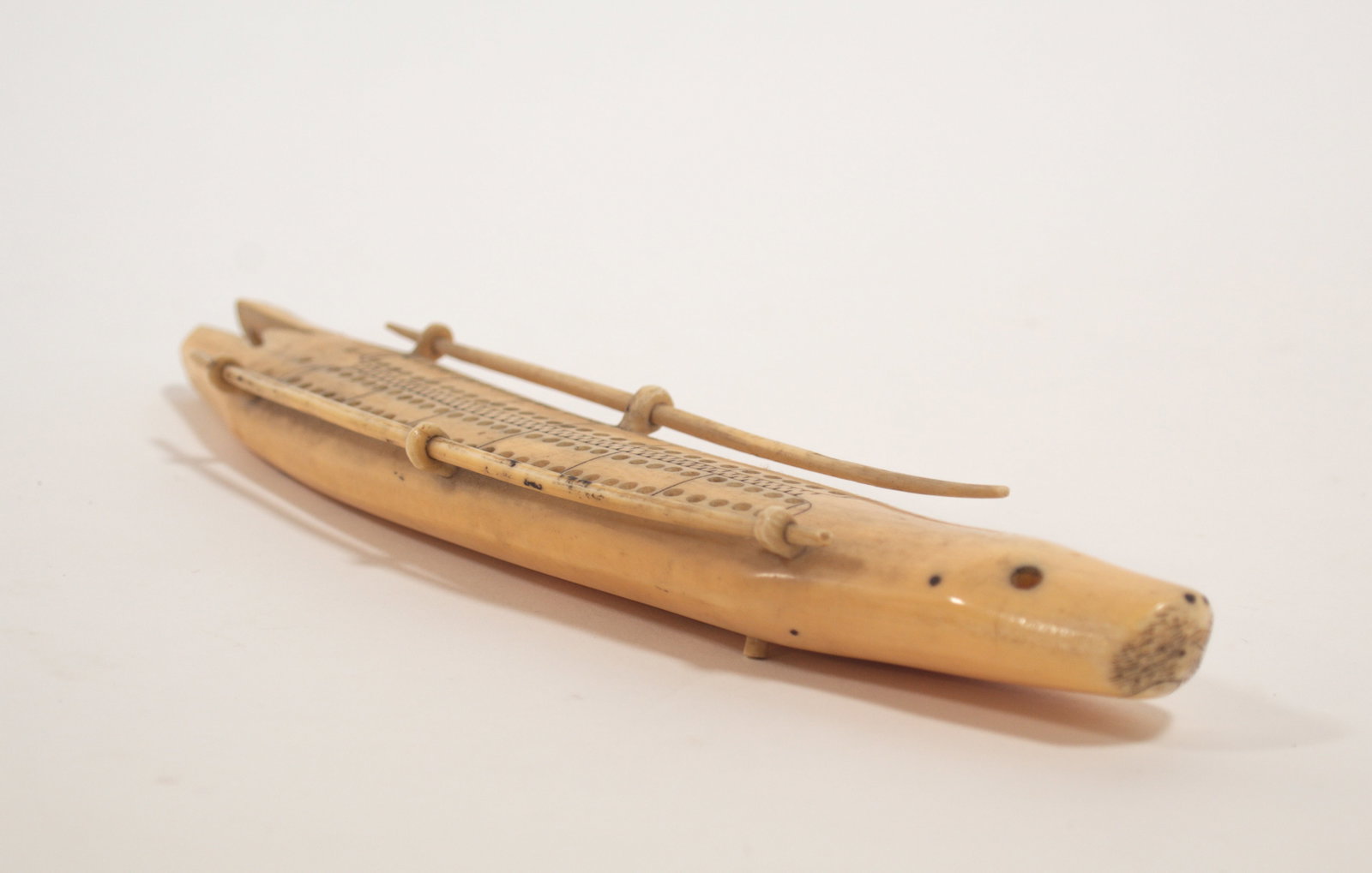 NATIVE AMERICAN CARVED SCRIMSHAW WALRUS TUSK CRIBBAGE BOARD IN THE FORM OF A SEAL KAYAK.: NATIVE AMERICAN CARVED SCRIMSHAW WALRUS TUSK CRIBBAGE BOARD IN THE FORM OF A SEAL KAYAK. Inuit/American, 19th Century. Seal-form kayak with scrimshaw mouth, whiskers, and nostrils, inset eyes (one