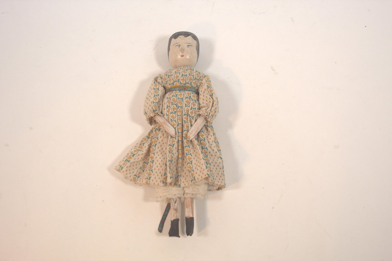 WOODEN GRODNERTAL PEG DOLL.: WOODEN GRODNERTAL PEG DOLL. European, early 20th Century. Having a jointed wood body with painted face, hair, and body, wearing a printed cotton dress, cotton and lace bloomers, and black painted