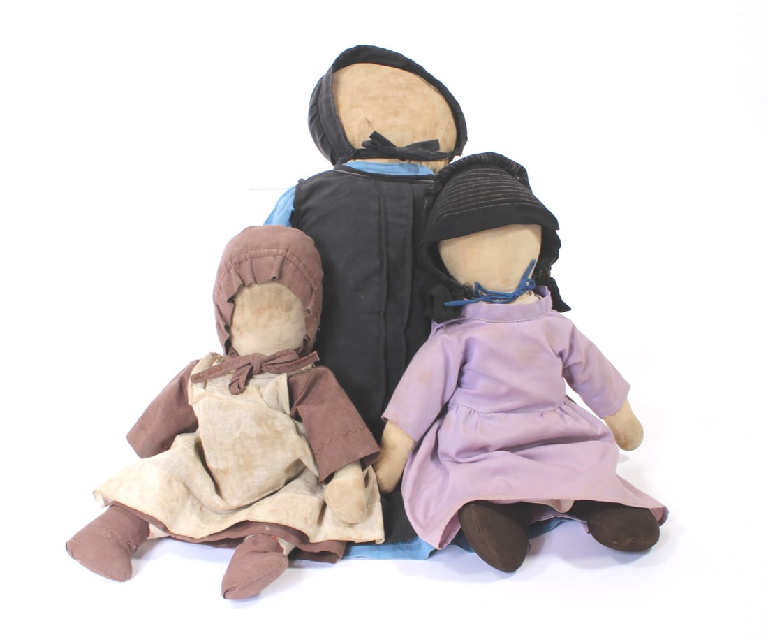 THREE AMISH DOLLS WEARING BONNETS.: THREE AMISH DOLLS WEARING BONNETS. American, early 20th Century. Faceless, soft body dolls. One in a lavender dress, black stockings, and wearing a black bonnet, 15"l. A jointed doll wearing a brown