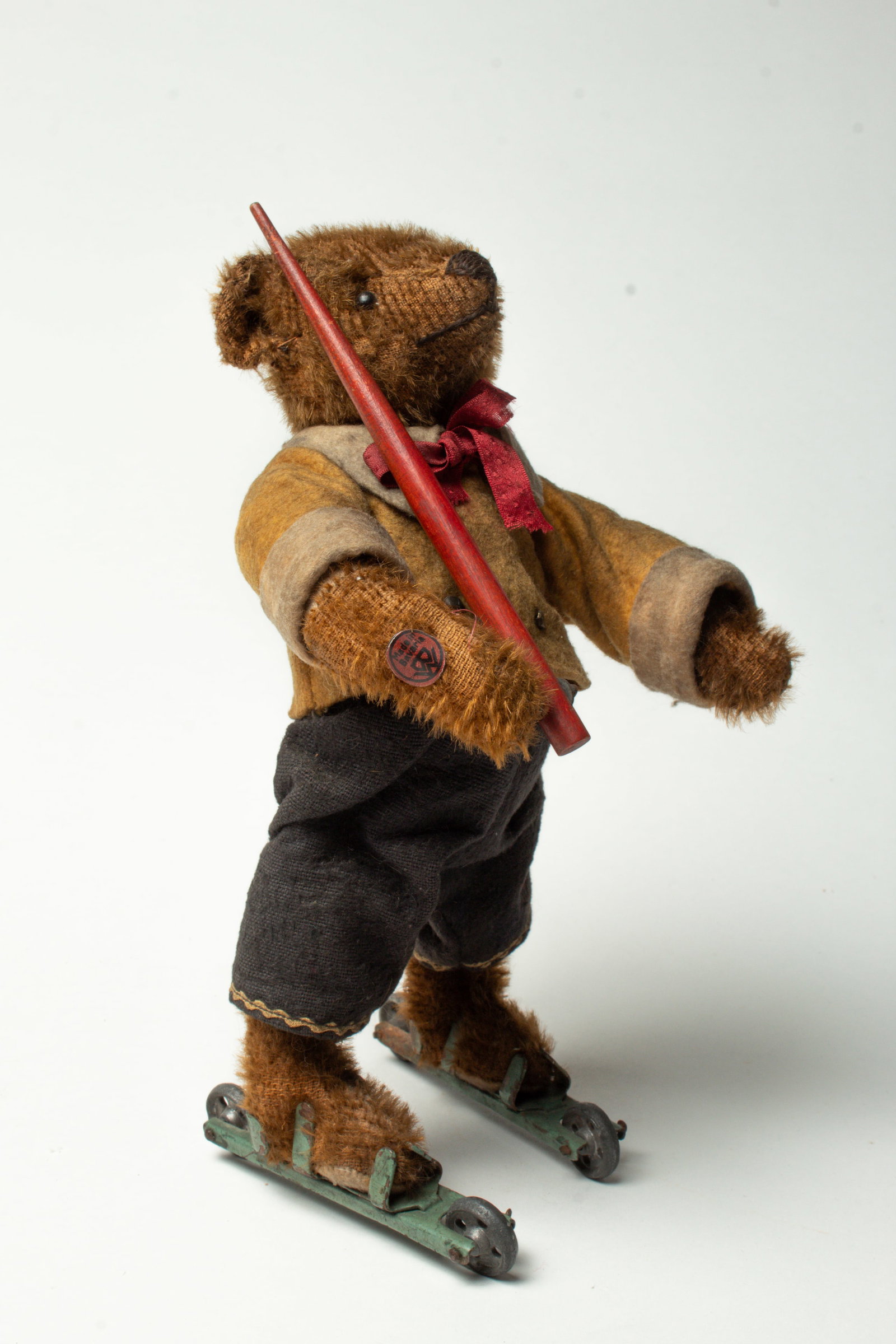 MECHANICAL BING BEAR ON ROLLER SKATES.: MECHANICAL BING BEAR ON ROLLER SKATES. Germany, early 20th Century. A mohair teddy bear wearing a yellow felt coat with white cuffs, blue pants, a red ribbon around its neck, on roller skates, and