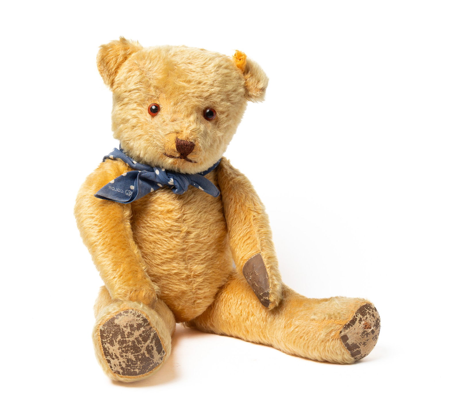 GOLDEN MOHAIR ARTICULATED TEDDY BEAR.: GOLDEN MOHAIR ARTICULATED TEDDY BEAR. American, early 20th Century. A straw-stuffed mohair bear with stick pin glass eyes, yarn nose and mouth, oil cloth pads, and wearing a blue and white polkadot