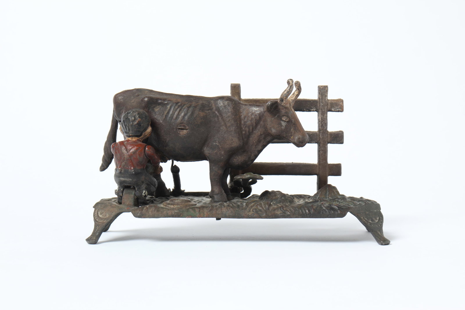 MILKING COW CAST IRON MECHANICAL BANK BY J & E STEVENS.: MILKING COW CAST IRON MECHANICAL BANK BY J & E STEVENS. American, late 19th Century. Depicts a man milking a cow near a fence on a four-legged base. 5.25"h. 9.75"l. 3.25"d.