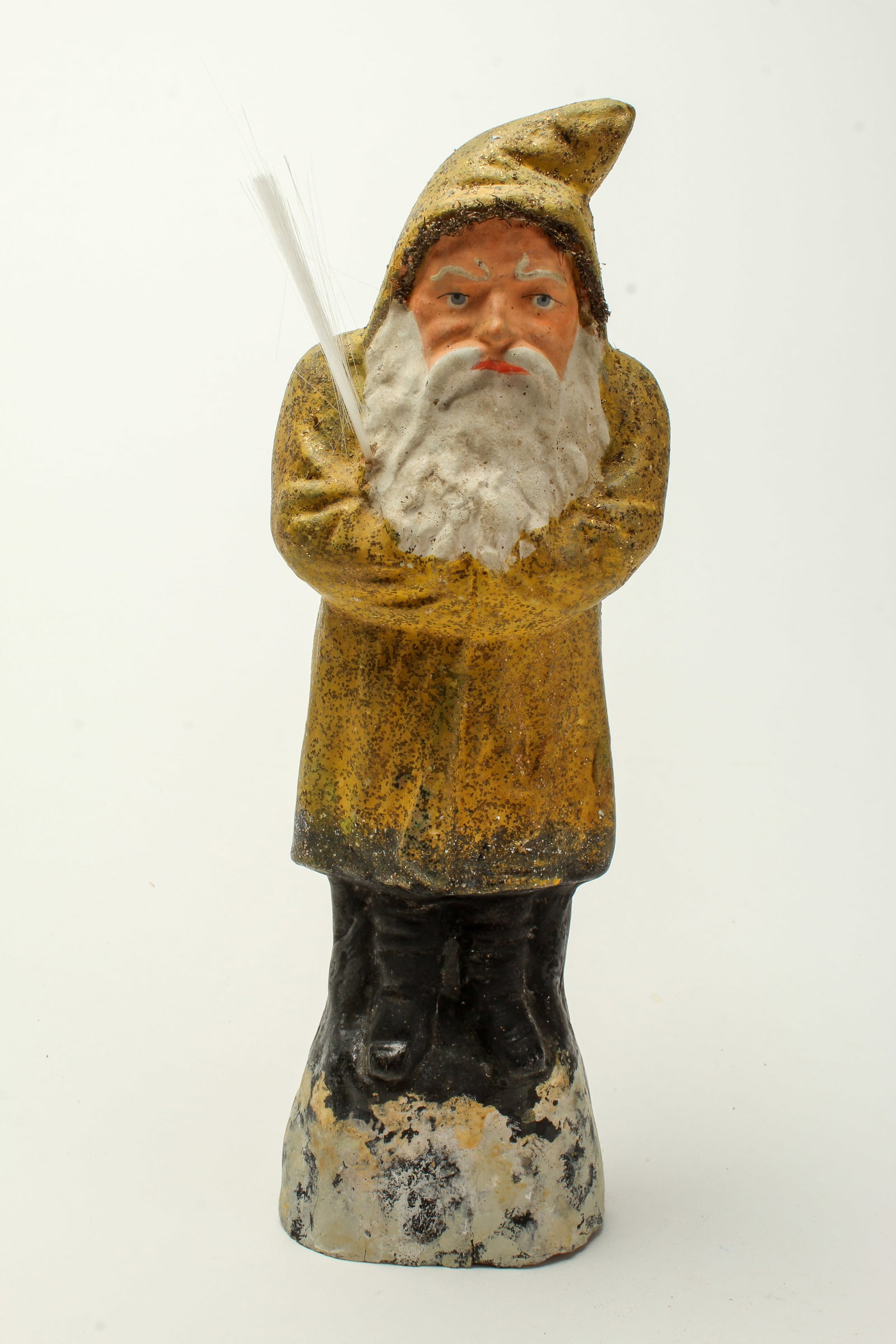GOLD COAT BELSNICKEL.: GOLD COAT BELSNICKEL. Germany, early 20th Century. Papier mache Belsnickel with a gold sparkly hooded coat, long white beard, on a black and white, and holding a spun glass. 12"h. Provenance: Nancy