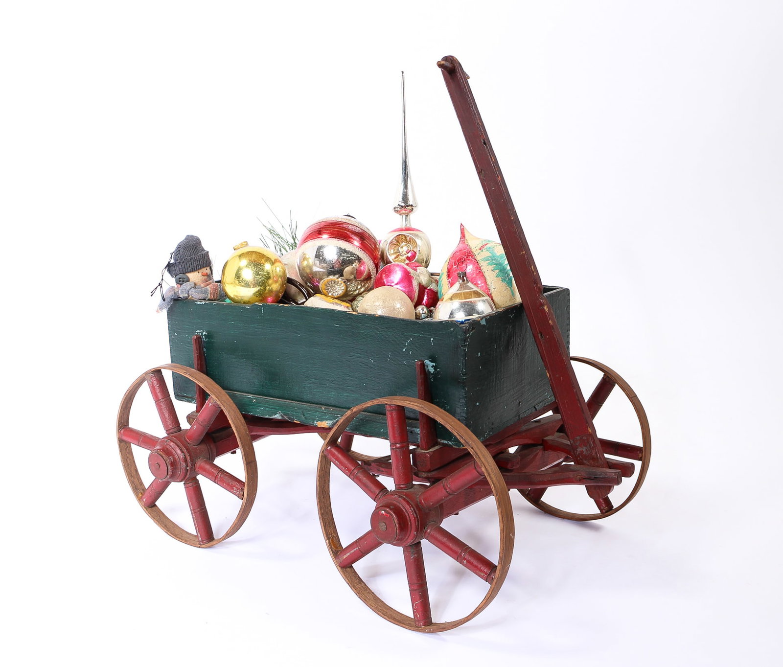 PAINTED CHILD'S DOLL WAGON FILLED WITH EARLY GLASS ORNAMENTS.: PAINTED CHILD'S DOLL WAGON FILLED WITH EARLY GLASS ORNAMENTS. American, 20th Century. A red and green painted wagon with a removable carriage, and wooden spoked wheels, filled with glass ornaments in 