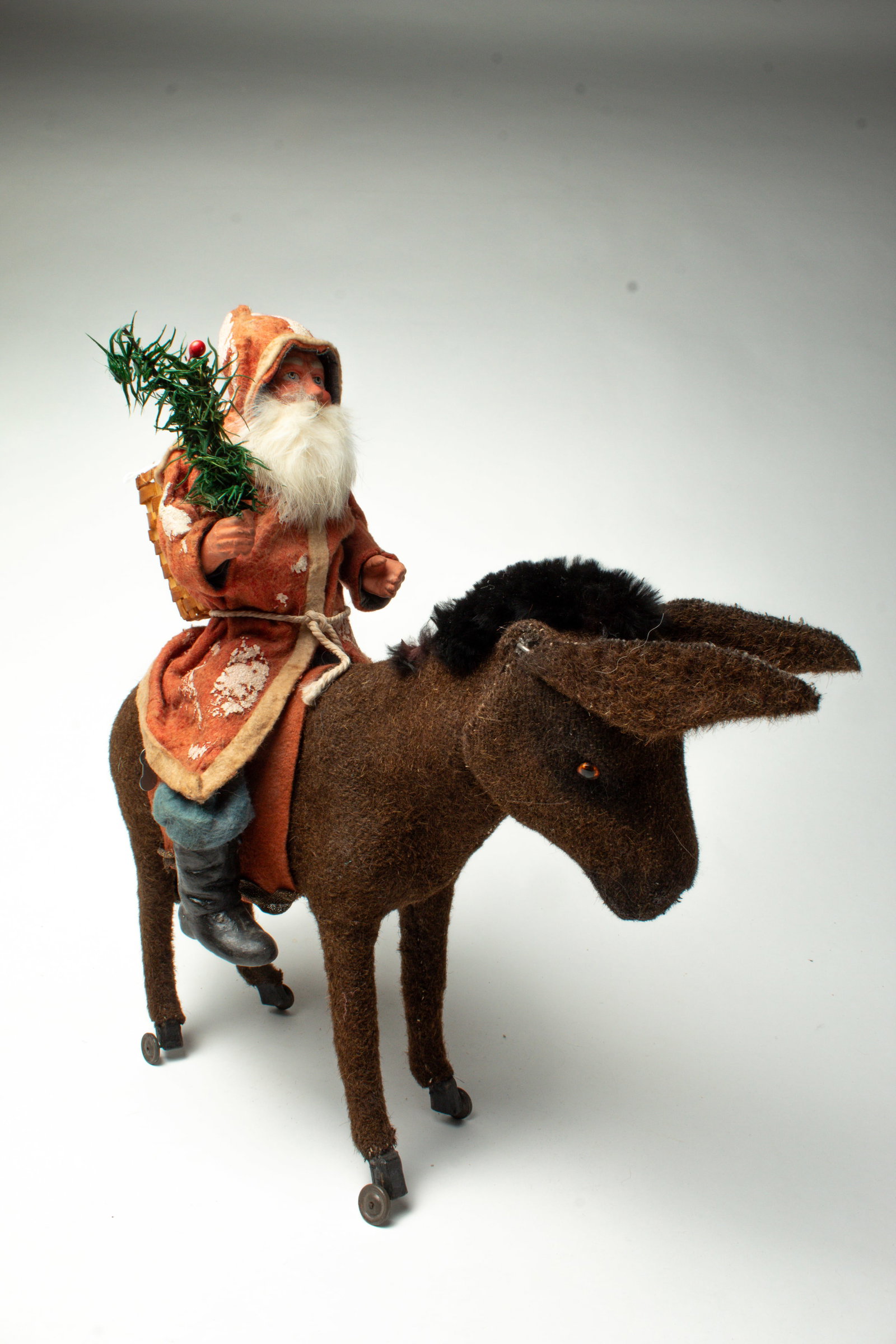 SANTA RIDING A MECHANICAL DONKEY.: SANTA RIDING A MECHANICAL DONKEY. Germany, early 20th Century. Santa has a rabbit fur beard, a composition face and hands, wearing a red hooded coat with white trim, blue pants, a basket strapped to