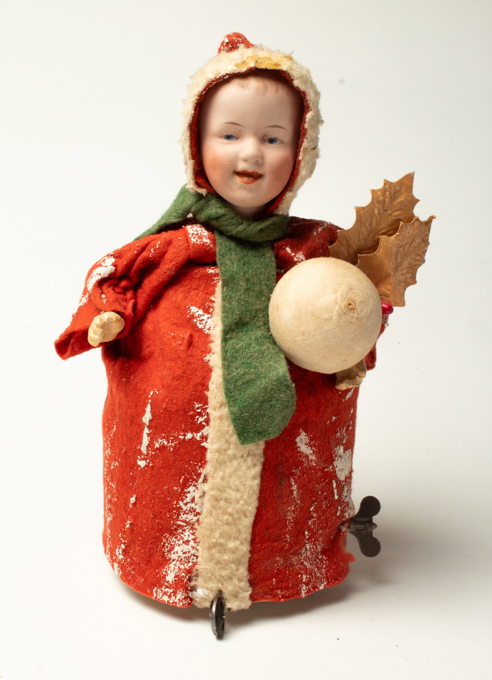 MECHANICAL CHRISTMAS DOLL HOLDING A SNOWBALL.: MECHANICAL CHRISTMAS DOLL HOLDING A SNOWBALL. Germany, early 20th Century. A bisque head doll with painted features, wearing a long red felt coat with white lining, a green scarf, holding a large