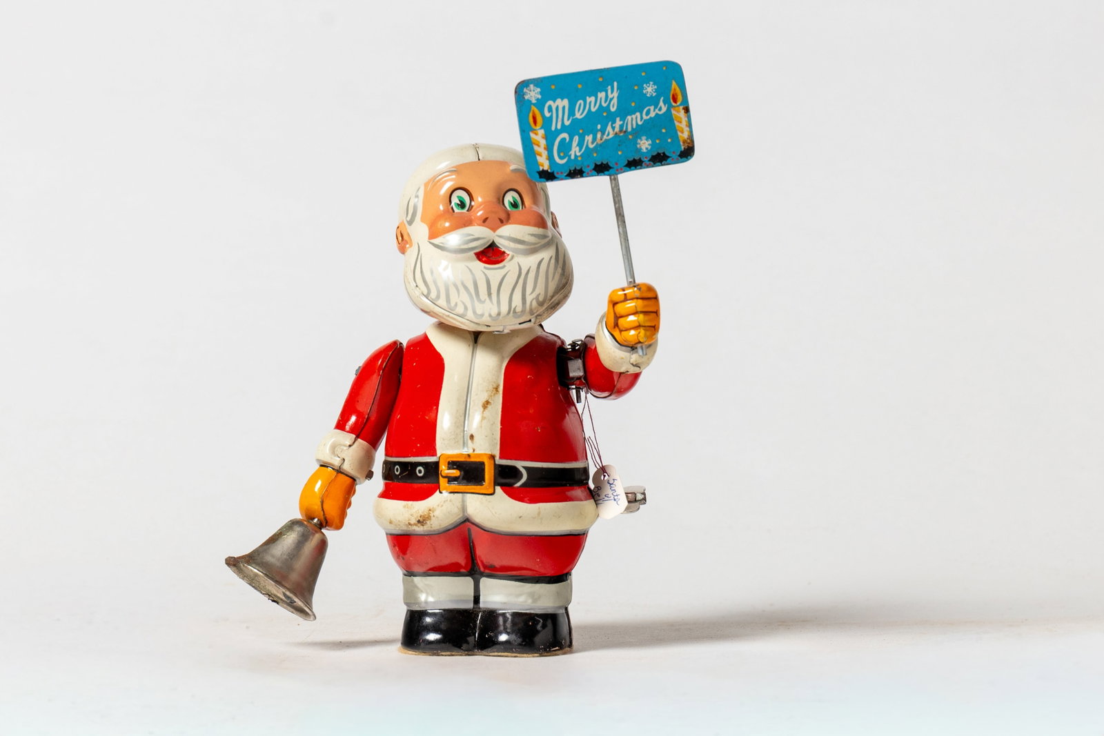 MECHANICAL TIN SANTA FIGURE.: MECHANICAL TIN SANTA FIGURE. Japanese, early 20th Century. A standing Santa holding a blue Merry Christmas sign in his left hand and a bell in his right. When wound up, Santa rings his bell and turns