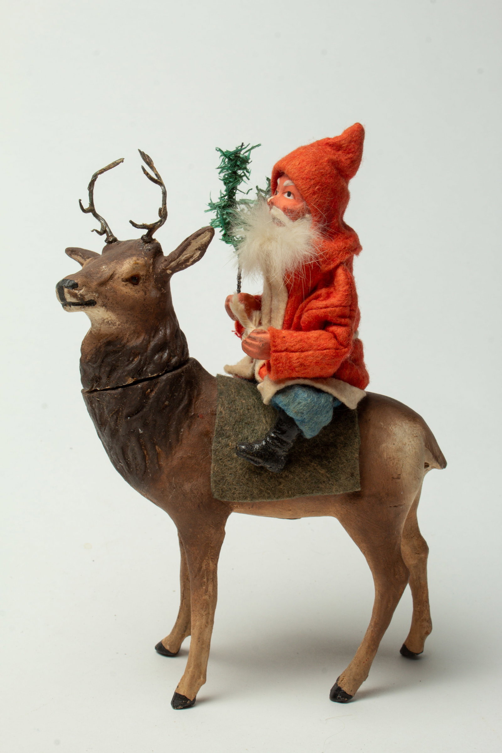 SANTA ON REINDEER CANDY CONTAINER.: SANTA ON REINDEER CANDY CONTAINER. Germany, early 20th Century. Santa wearing a red hooded coat, blue pants, black boots, with a fur beard, composition hands and face, and holding a feather tree
