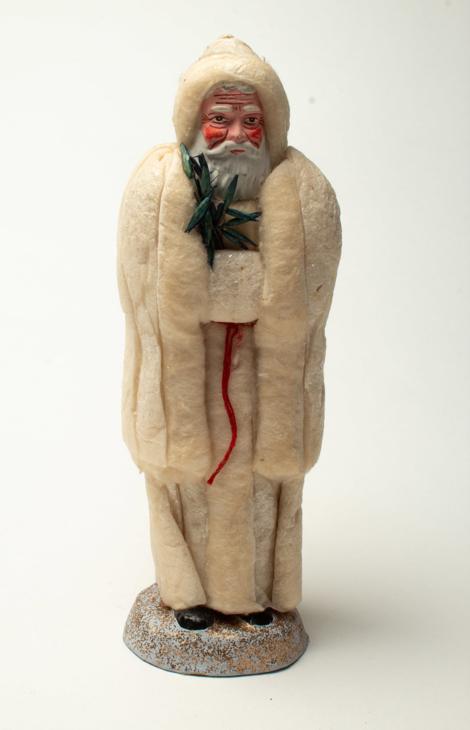 COTTON COAT SANTA CANDY CONTAINER.: COTTON COAT SANTA CANDY CONTAINER. France, early 20th Century. A white cotton batting coat and muff, a red string belt, holding a tree made of oats, and with a painted wooden face. Santa is on a blue