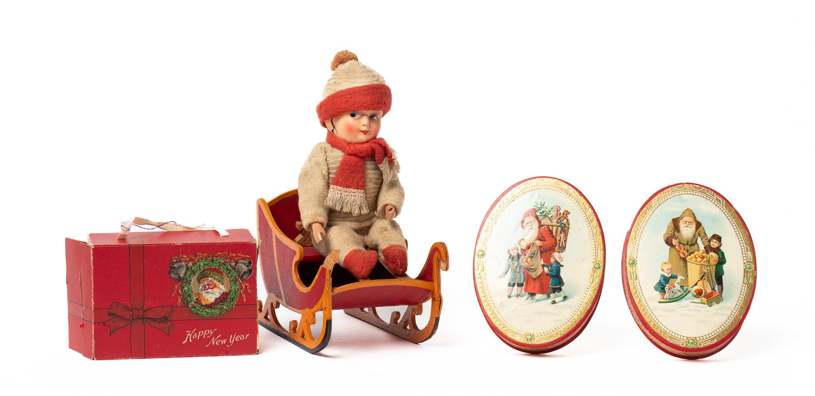 BOY ON SLED CANDY CONTAINER AND THREE EARLY PAPER CHRISTMAS BOXES.: BOY ON SLED CANDY CONTAINER AND THREE EARLY PAPER CHRISTMAS BOXES. Germany, early 20th Century. A seated boy wearing a white outfit with red trim, a matching scarf and hat, with a painted composition 