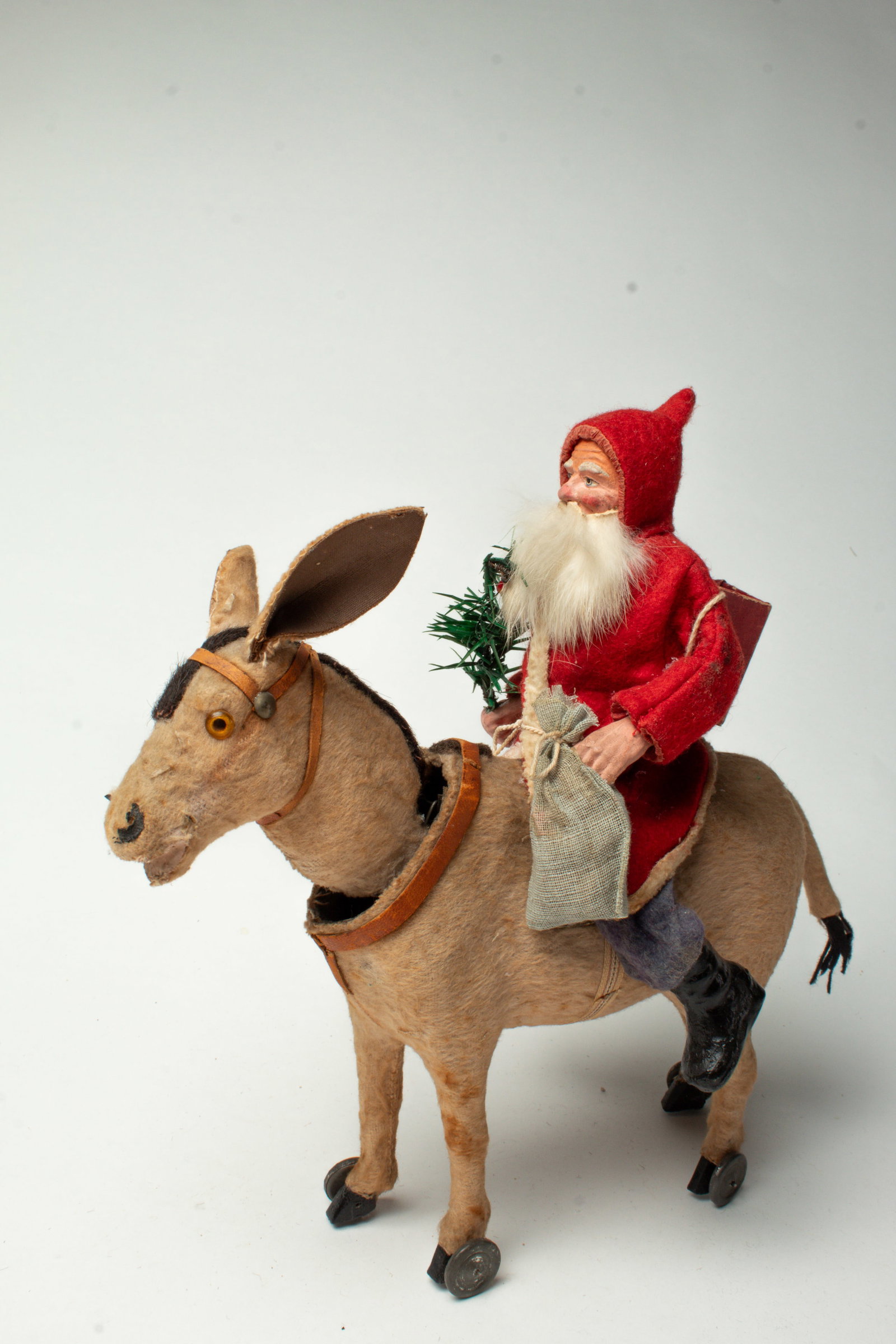 SANTA RIDING A NODDING REINDEER.: SANTA RIDING A NODDING REINDEER. Germany, early 20th Century. Santa in a hooded red coat with white trim, blue pants and black boots, a composition face with a rabbit fur beard, and is holding a feath