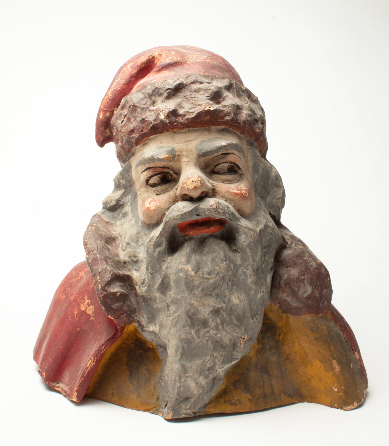 PAPIER MACHE SANTA BUST.: PAPIER MACHE SANTA BUST. German or American. Bust of Santa with a red hat, red cloak over a gold top, with his long beard and eyes looking off to the side. 16"h. 16"w. Provenance: Nancy Goff (Alliance