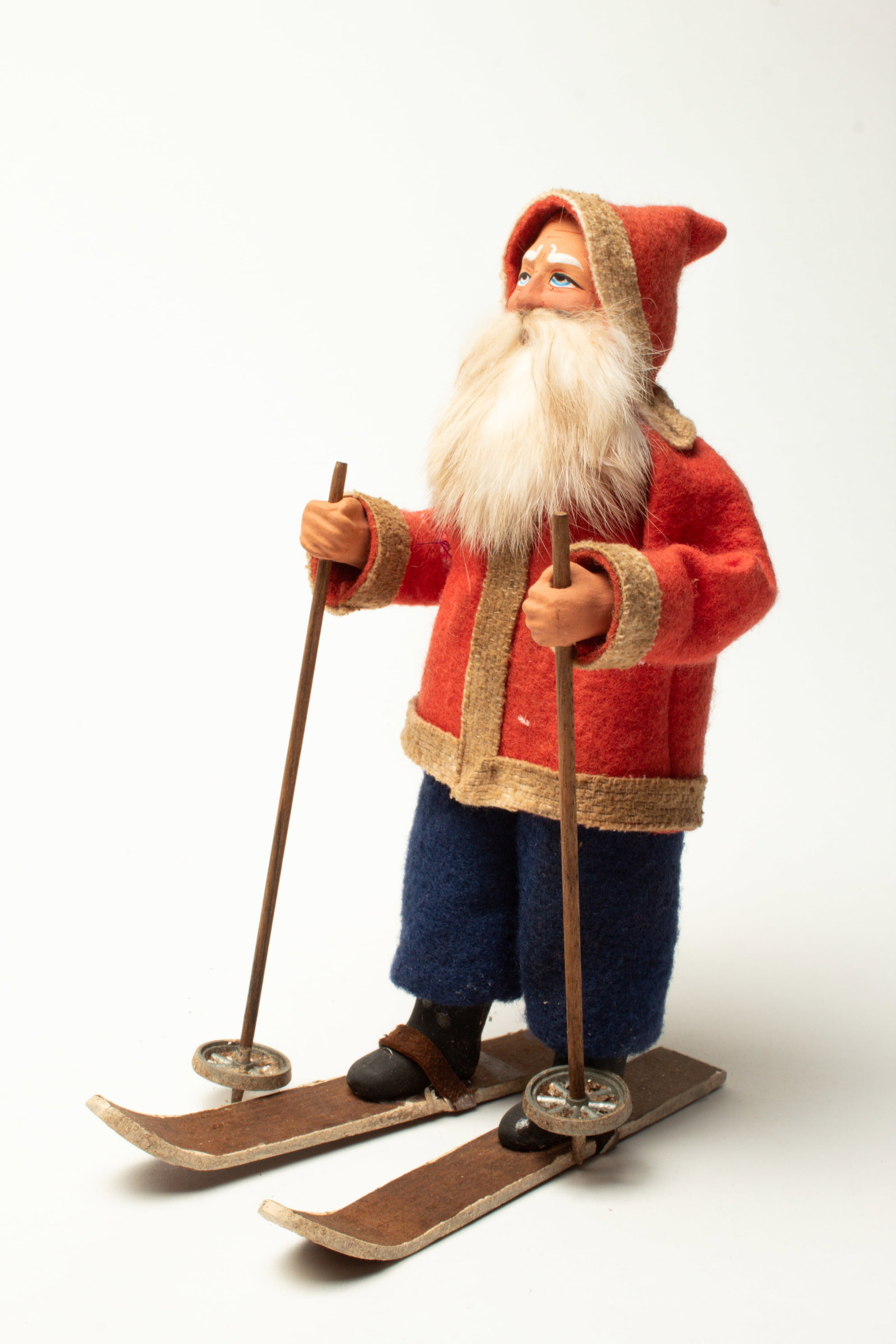 SKIING SANTA FIGURE.: SKIING SANTA FIGURE. Germany, early 20th Century. A Santa with a composition face, rabbit fur beard, wearing a hooded red coat with white trim, blue pants, black boots, and on wooden skis with ski