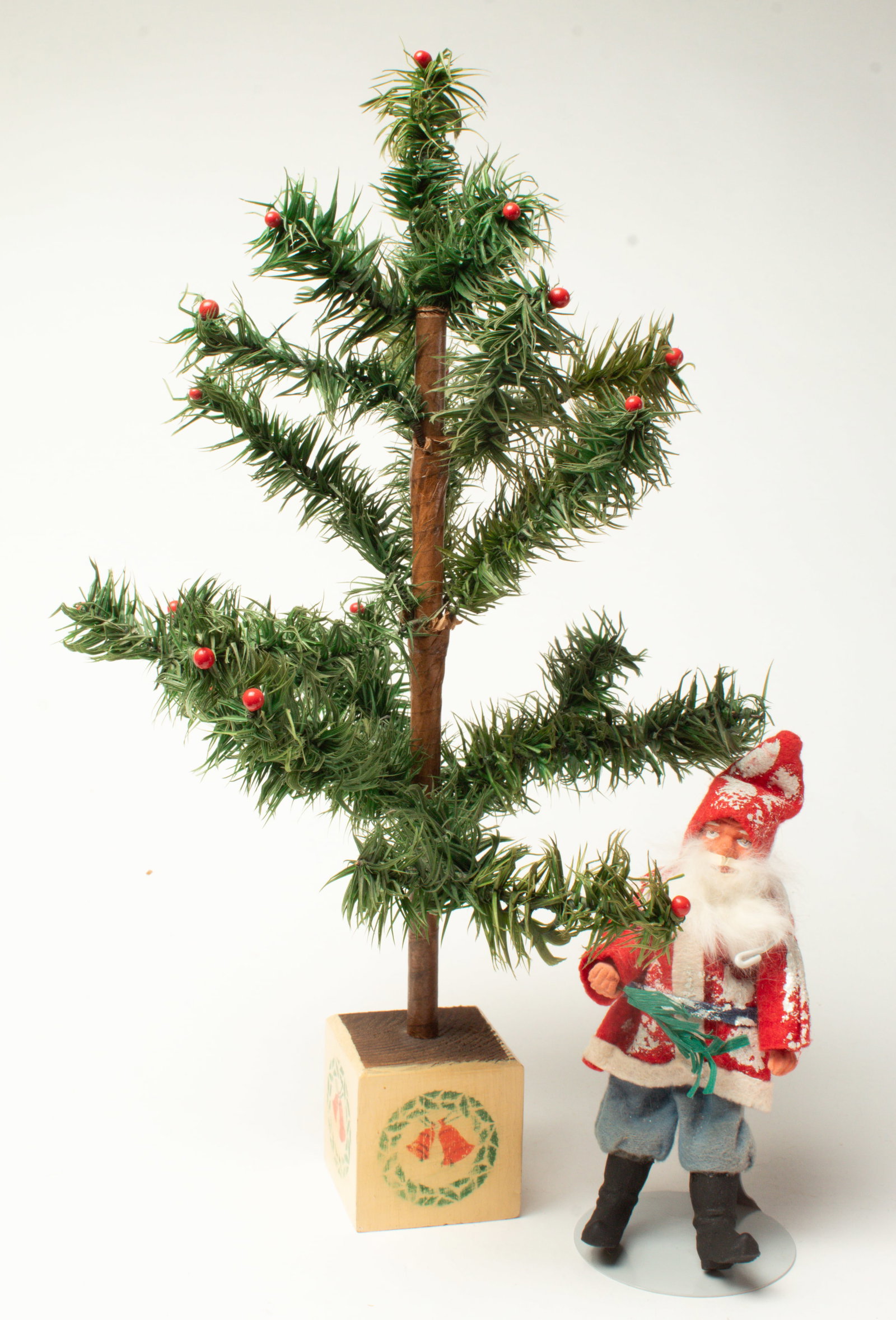 SANTA FIGURE WITH A DIMINUTIVE FEATHER TREE.: SANTA FIGURE WITH A DIMINUTIVE FEATHER TREE. Germany, early 20th Century. A Santa figure with a wire and peg body, a composition face and hands, and feet wearing a short red coat with white trim,