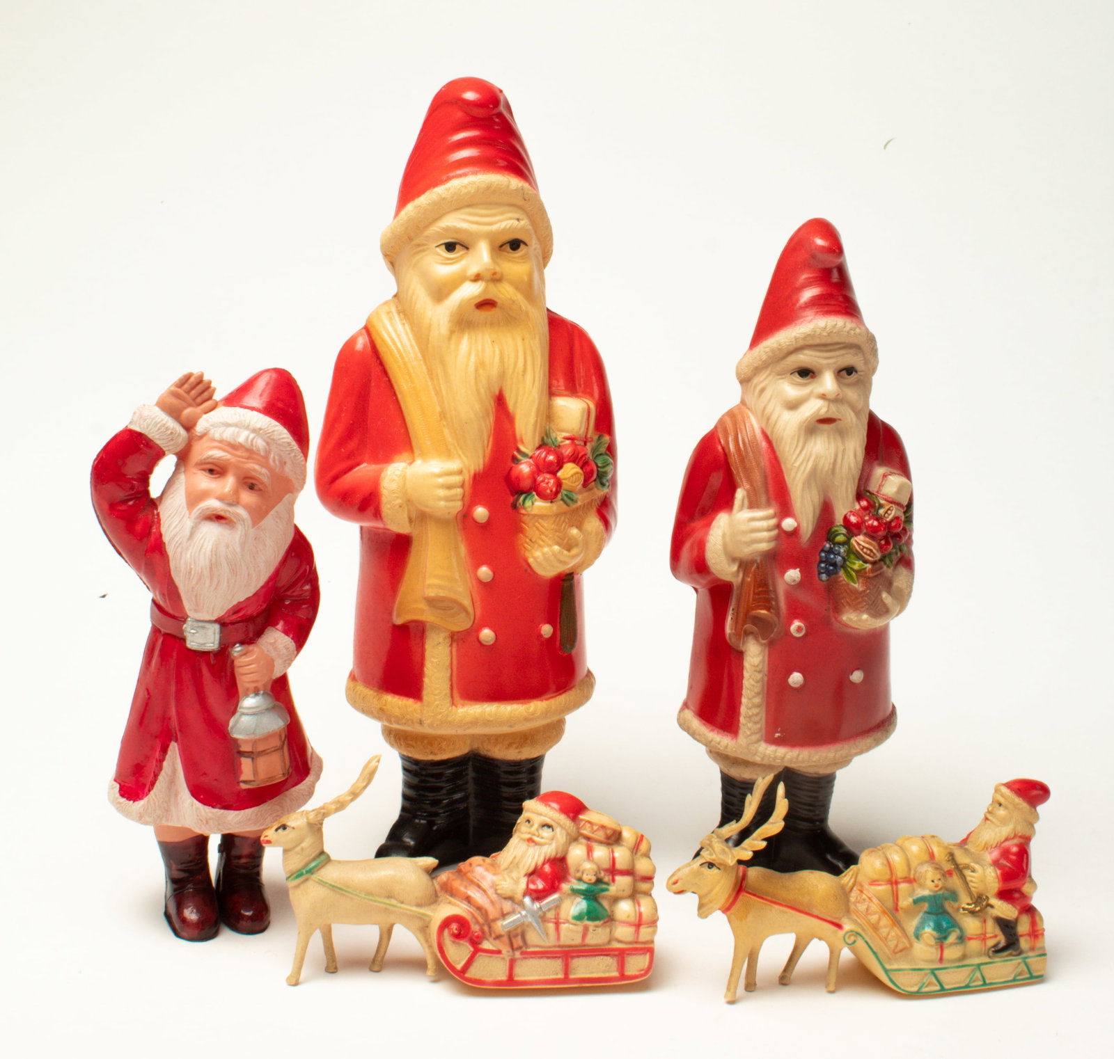 GROUP OF CELLULOID SANTA FIGURES.: GROUP OF CELLULOID SANTA FIGURES. American and Japanese, 20th Century. Two diminutive Santas on sleighs, both being pulled by reindeer and sleds full of toys, and three standing Santa figures; one