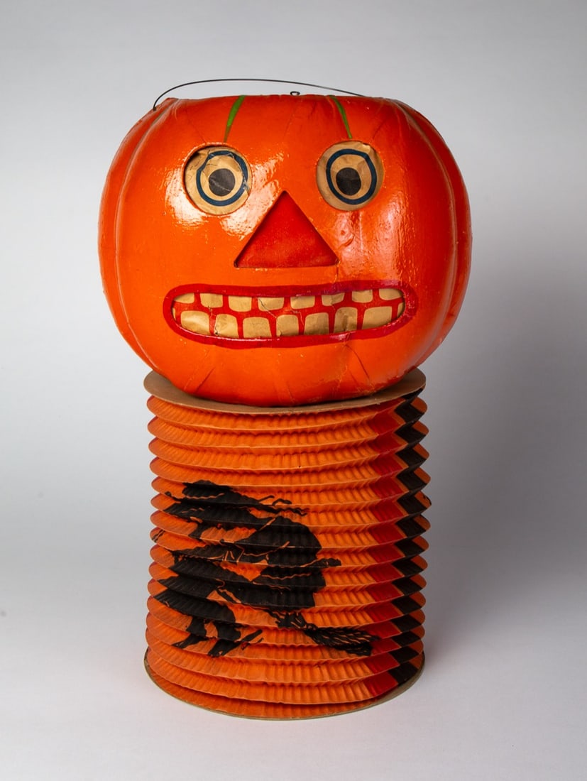 HALLOWEEN JACK-O-LANTERN WITH ACCORDION BOTTOM.: HALLOWEEN JACK-O-LANTERN WITH ACCORDION BOTTOM. Germany, 20th Century. Orange with green veins at top along with bull's-eye eyes and red nose; having a wire bail; accordion with witch and bat; 17"h.