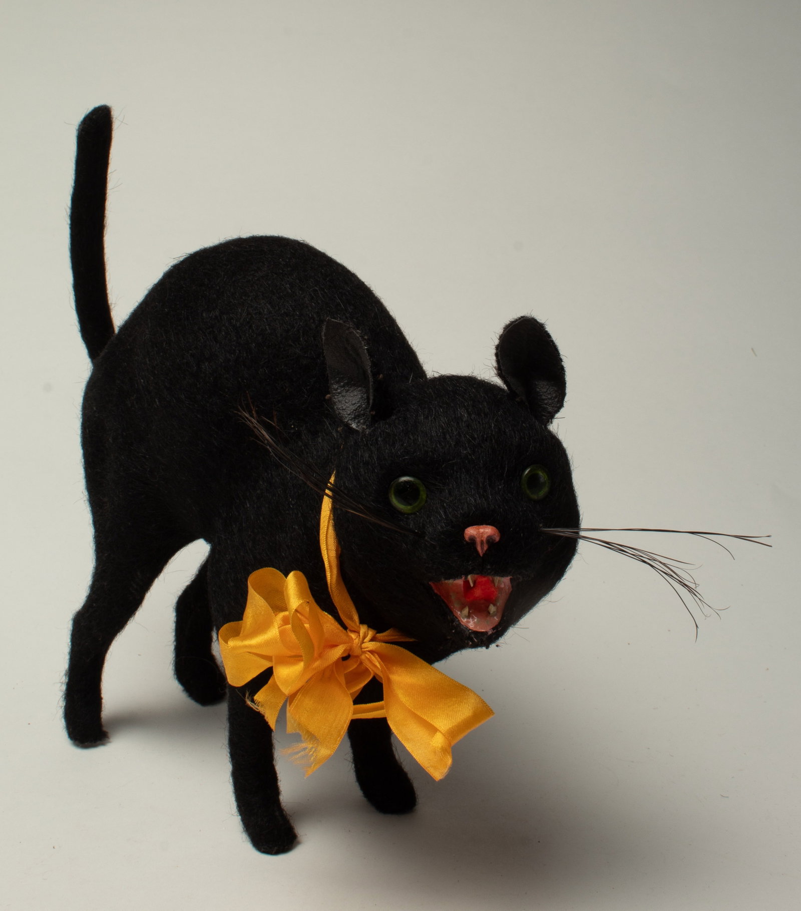 BLACK CAT CANDY CONTAINER.: BLACK CAT CANDY CONTAINER. Germany, early 20th Century. A black cat standing with a hunched back, pink nose, an open hissing mouth, green glass eyes, and a gold ribbon around its neck. He has a