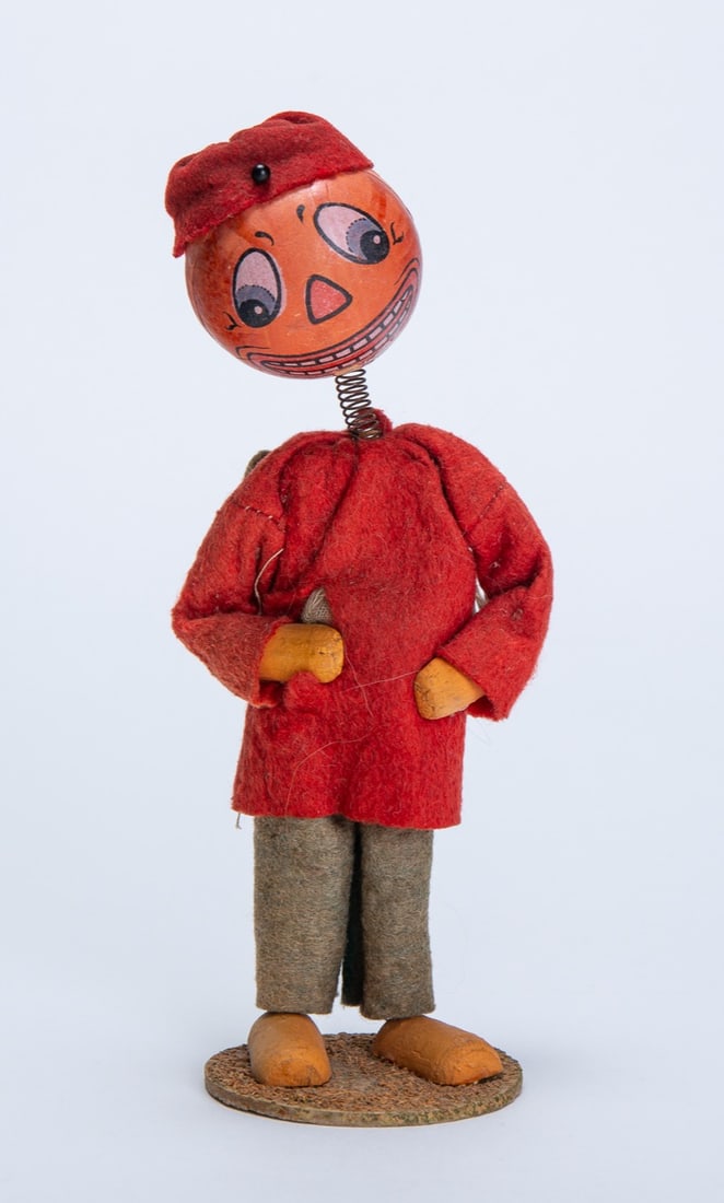 PUMPKIN MAN HALLOWEEN NODDER WITH CANDY CONTAINER BACKPACK.: PUMPKIN MAN HALLOWEEN NODDER WITH CANDY CONTAINER BACKPACK. Germany, 20th Century. Depicting a pumpkin man whose head is attached to a long spring; wearing a red shirt, green pants, and candy containe