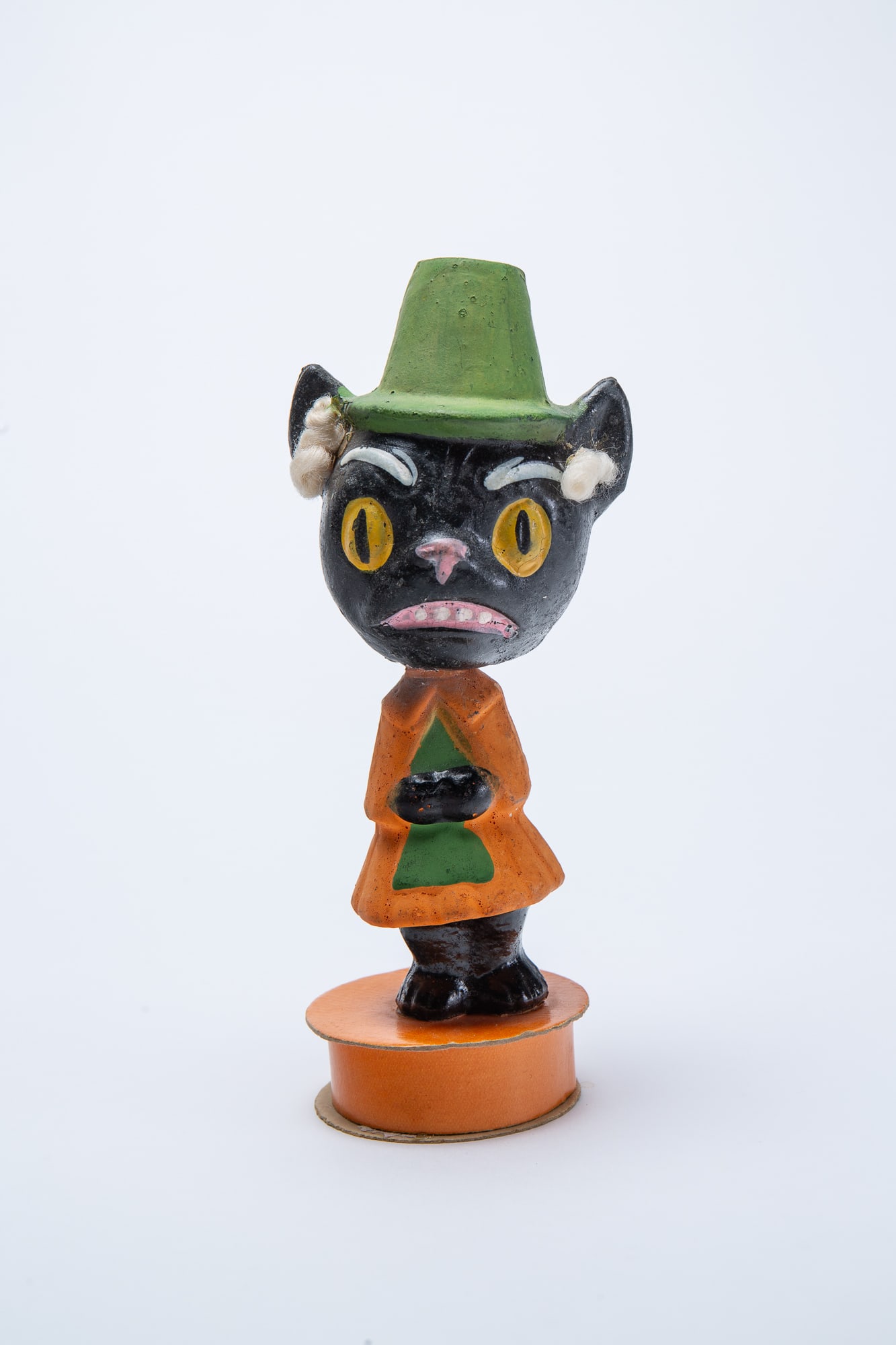 BLACK CAT HALLOWEEN CANDY CONTAINER NODDER.: BLACK CAT HALLOWEEN CANDY CONTAINER NODDER. Germany, early 20th Century. Depicting a standing composition cat with green hat, hair curls, and nodding head continuing to an orange dress; standing on a 