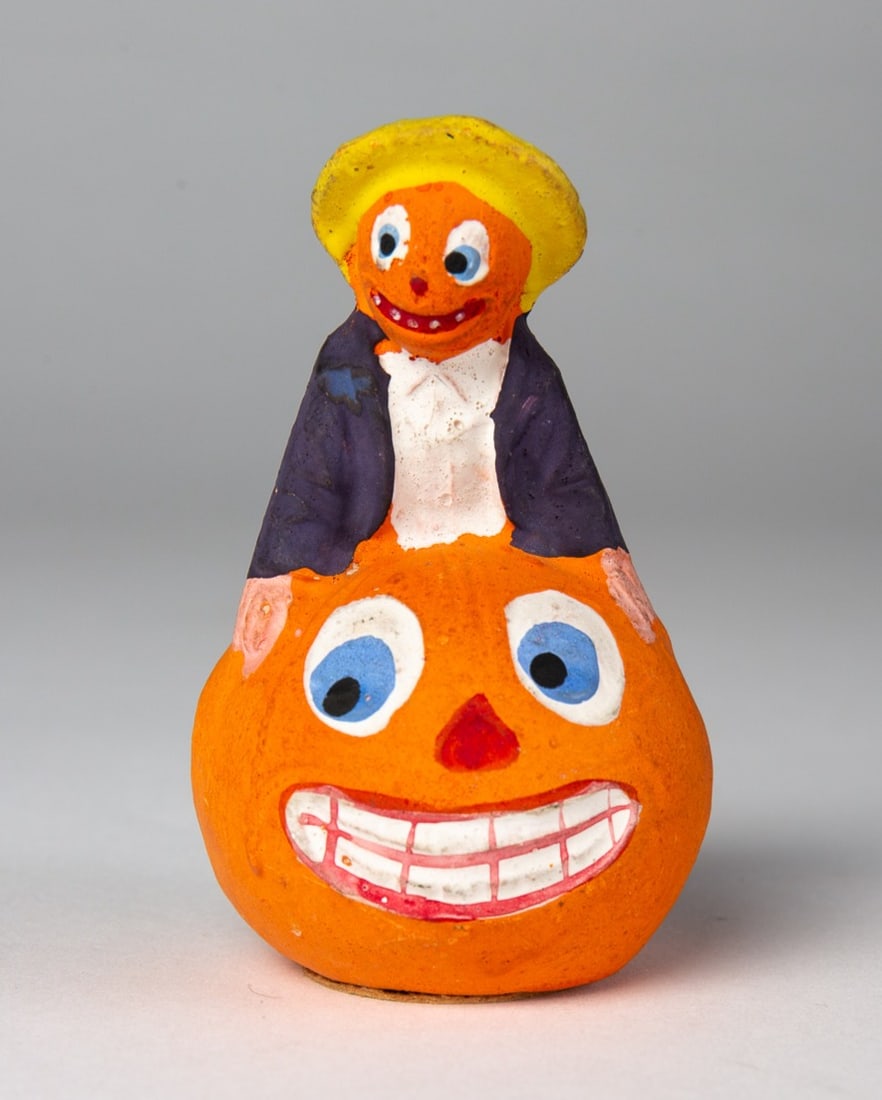 BOY SITTING ON PUMPKIN HALLOWEEN CANDY CONTAINER.: BOY SITTING ON PUMPKIN HALLOWEEN CANDY CONTAINER. Germany, 20th Century. Composition. Depicting a grinning pumpkin face with boy on top; boy with yellow hat, black coat, green pants, red stockings,