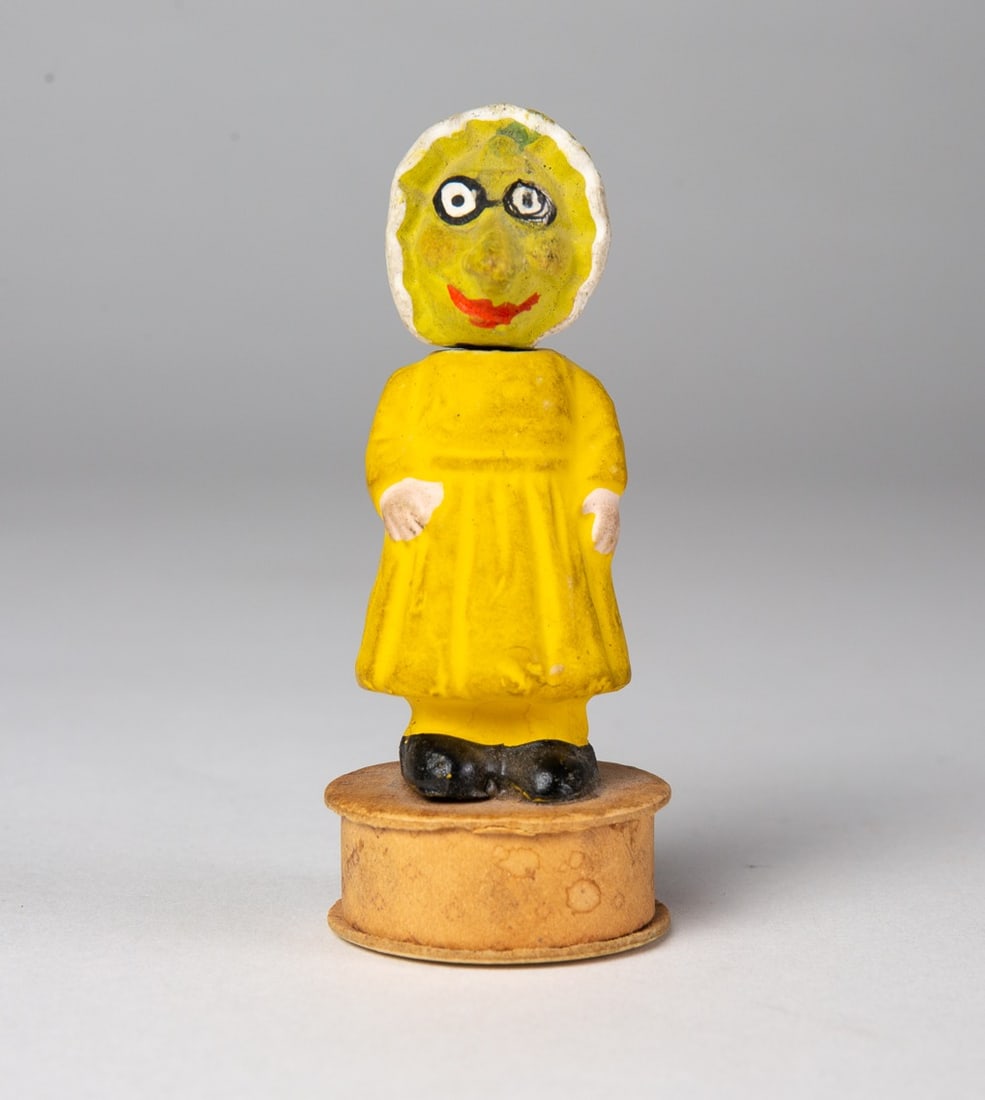 SQUASH LADY HALLOWEEN NODDER CANDY CONTAINER.: SQUASH LADY HALLOWEEN NODDER CANDY CONTAINER. Germany, 20th Century. Wearing a white bonnet, glasses, yellow dress, and white shoes; standing on a small, round candy box base with wallpaper; 3.5"h. 1.