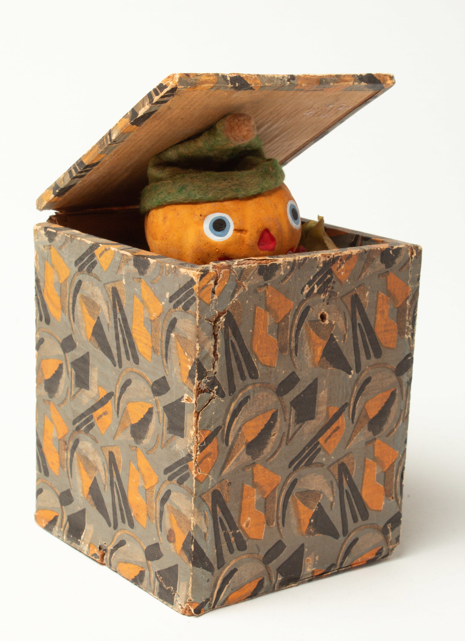JACK IN THE BOX PUMPKIN MAN.: JACK IN THE BOX PUMPKIN MAN. Germany, early 20th Century. A composition pumpkin head wearing a green felt hat, a red and green crepe paper clown collar, and inside a blue, black, and orange covered bo