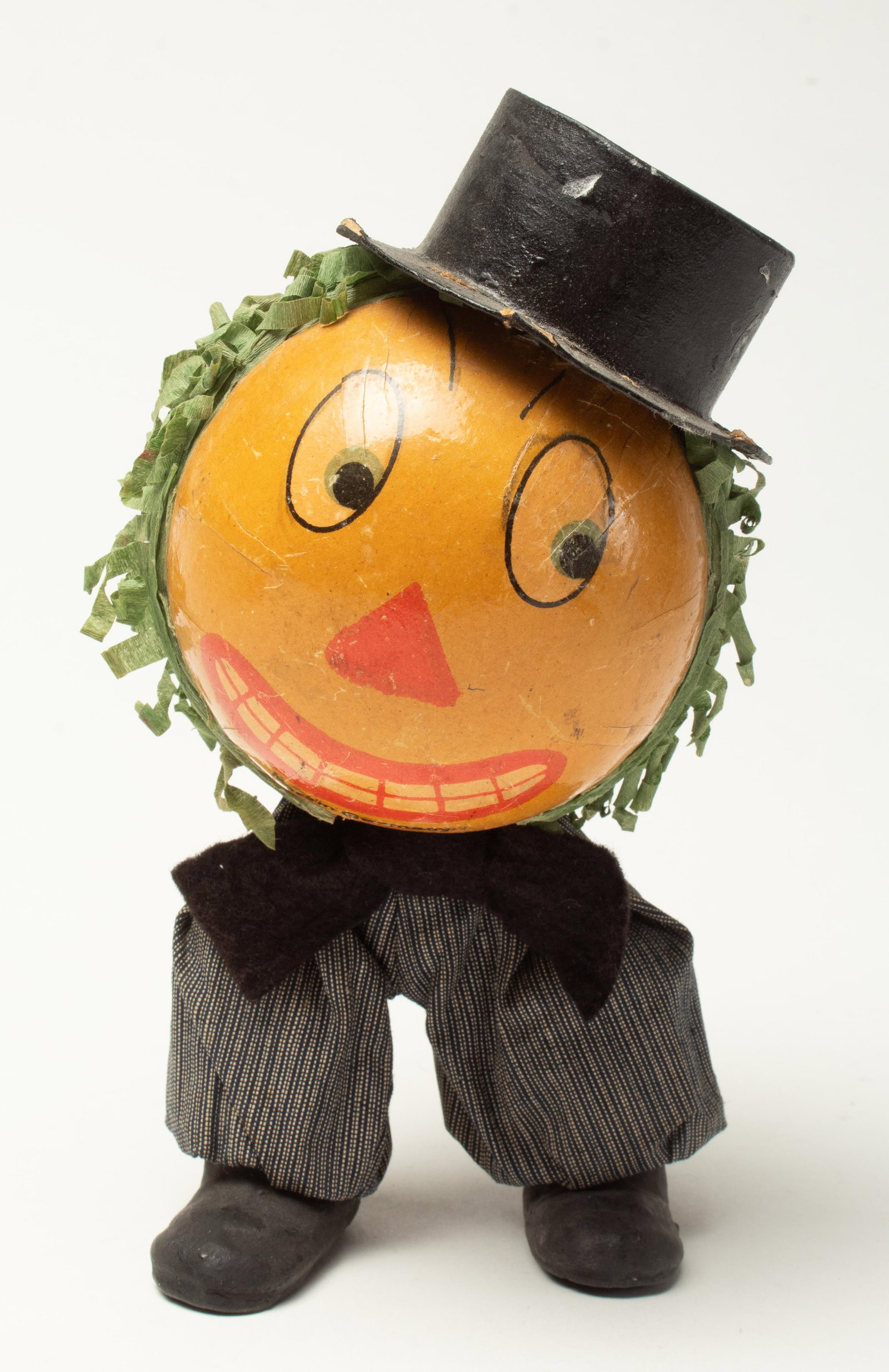 MECHANICAL WIND-UP PUMPKIN MAN.: MECHANICAL WIND-UP PUMPKIN MAN. Germany, early 20th Century. A large spherical pumpkin head with green crepe paper hair, wearing a black top hat, black striped pants, and black shoes. When you wind